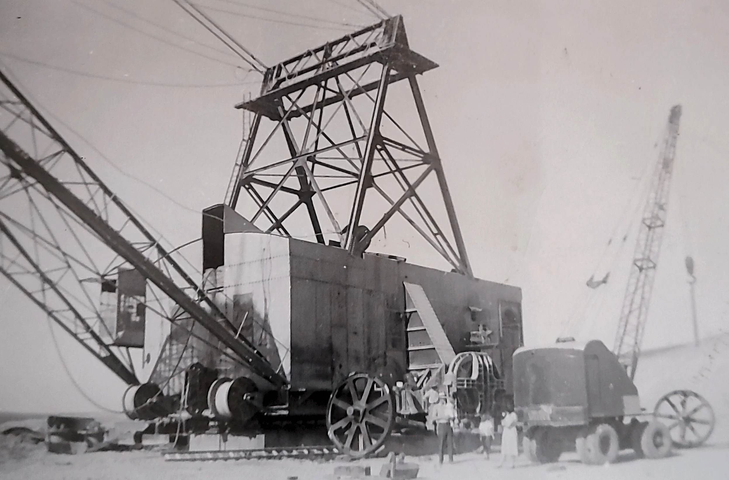 Black and white photograph of an early 20th-century large steel tower with a platform at the top, supporting electrical wires, and mounted on a wheeled base for mobility.