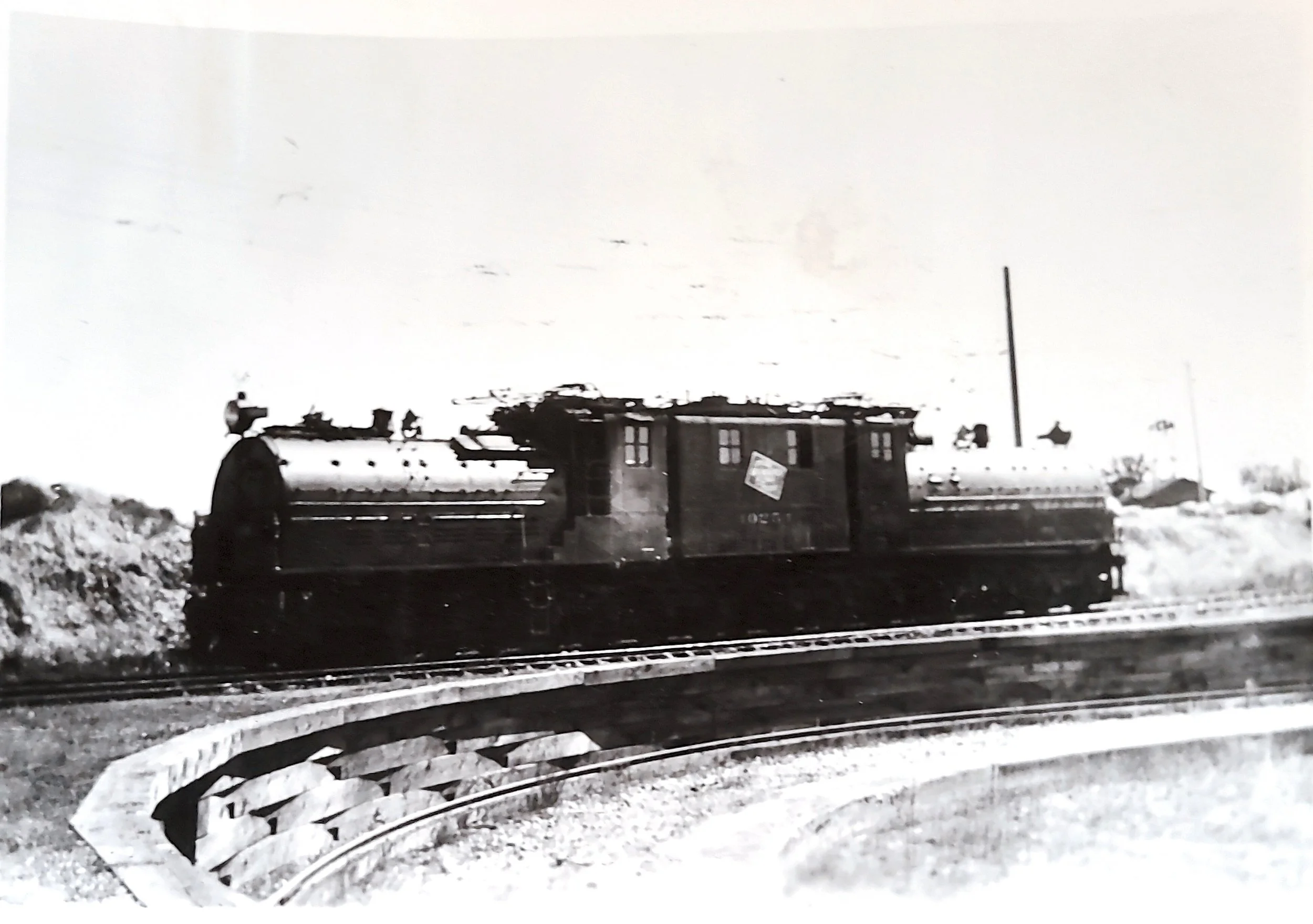 Black and white image of an old train on tracks, with a small building and snow on the ground.