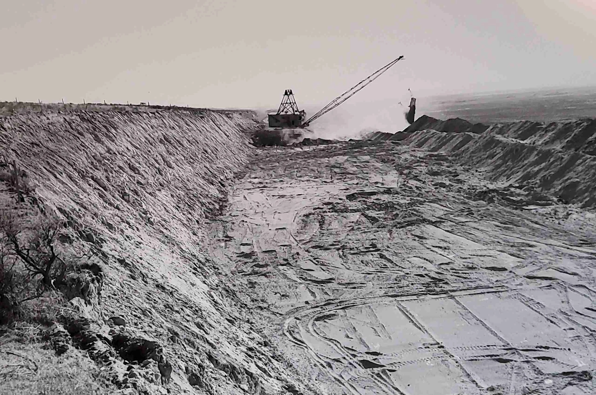 Historical black and white photo of Industrial crane digging a trench