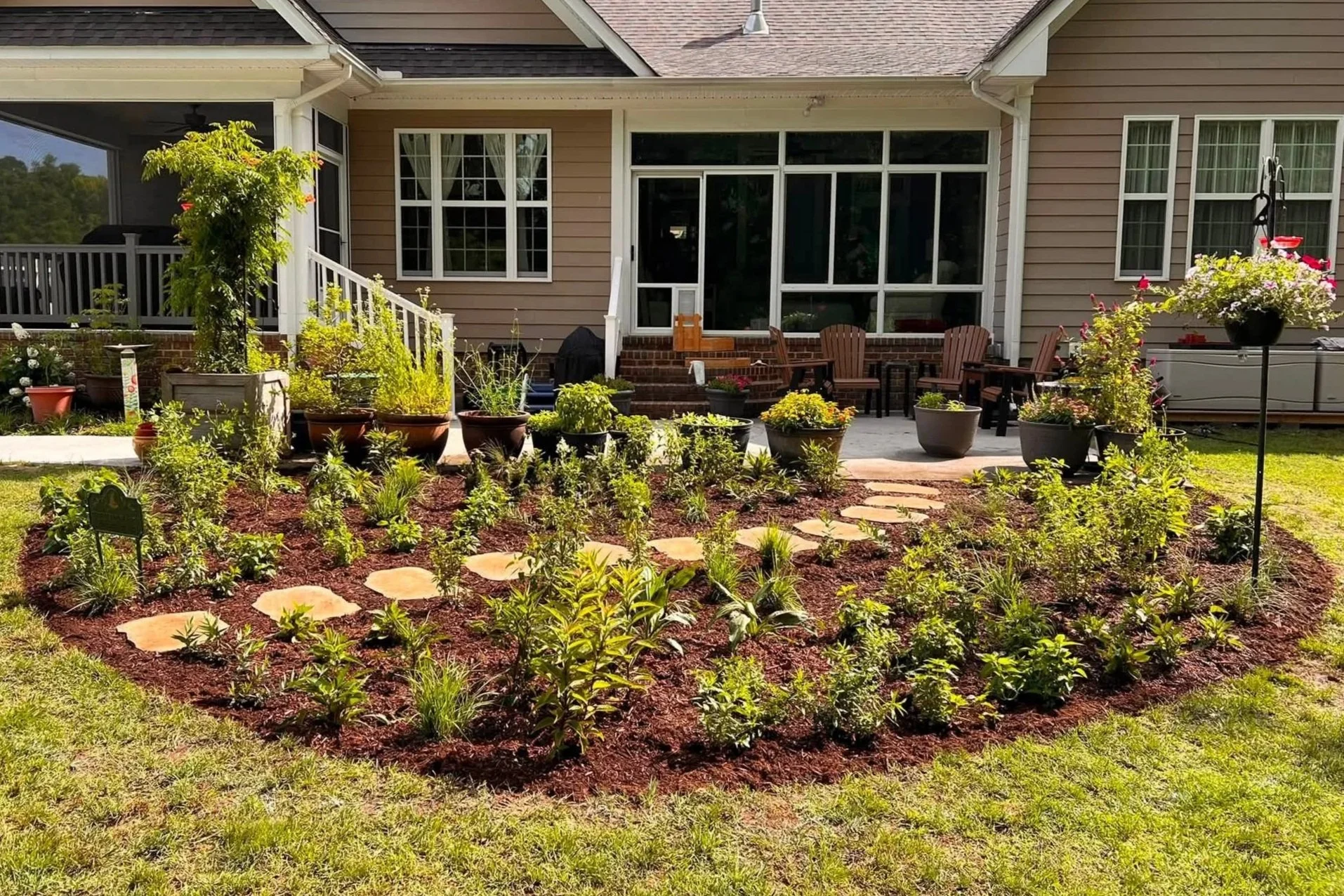 Evergreen Eco-Scapes Project; Ecological Landscaping; Backyard garden with a tiled path, potted plants, a wooden table with chairs, and a house with large windows and a porch.