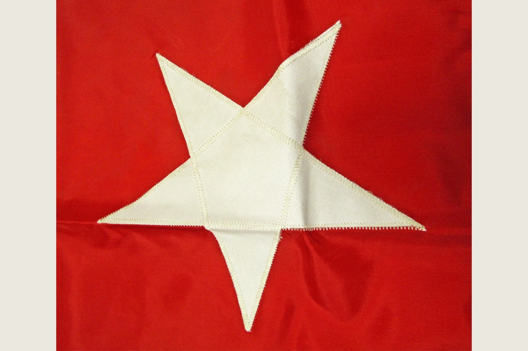 Close detail of one white appliqué star on the red headquarters flag.