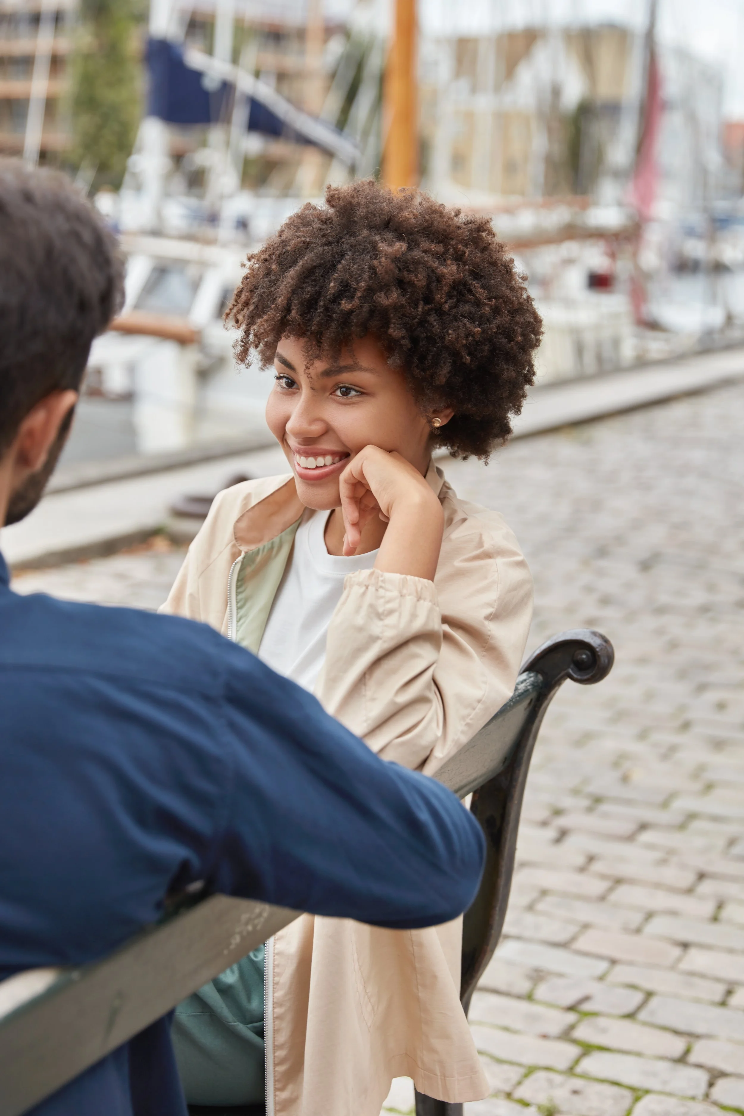 A man and woman sitting on a bench. The woman is smiling at the man.