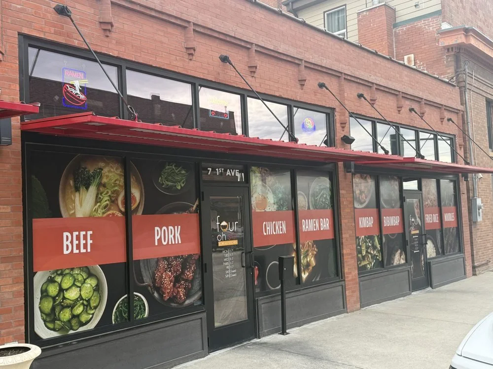 Exterior of a ramen restaurant with large windows displayingImages of ramen, vegetables, and meat, and red banners with menu items like beef, pork, chicken, and ramen bar.