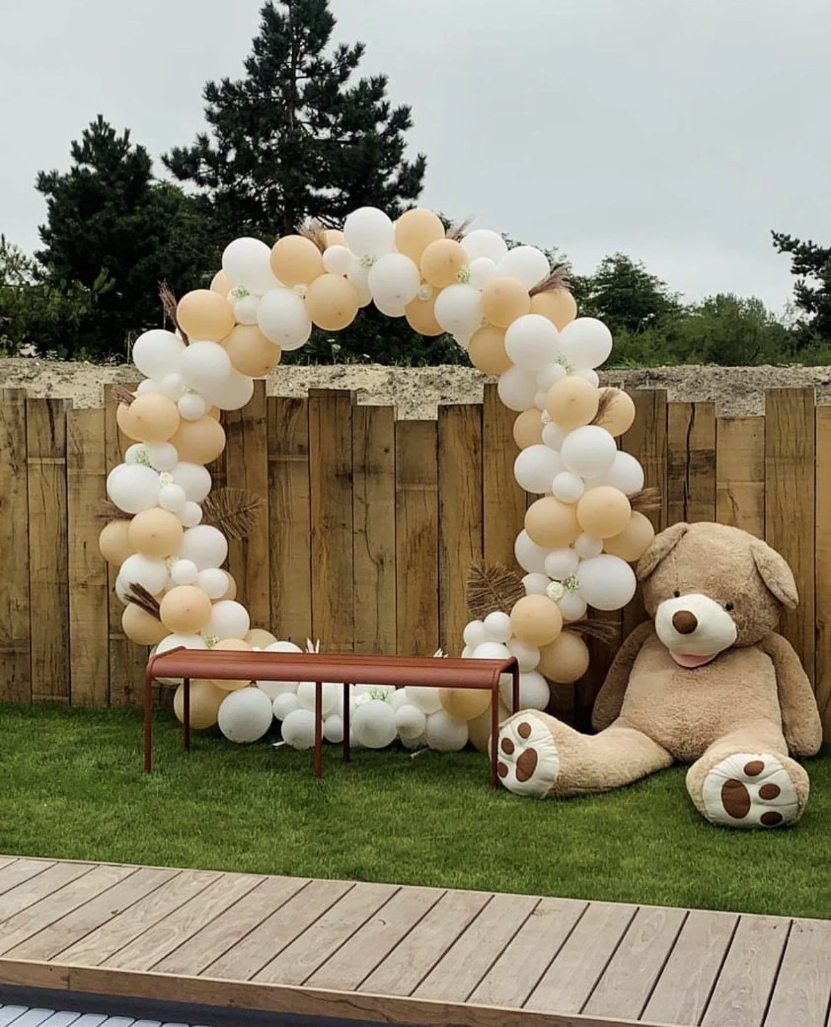 Décoration de baptême avec arche de ballons blanc, beige et doré, grand ours en peluche, petit escabeau en bois et décoration élégante pour coin photo.