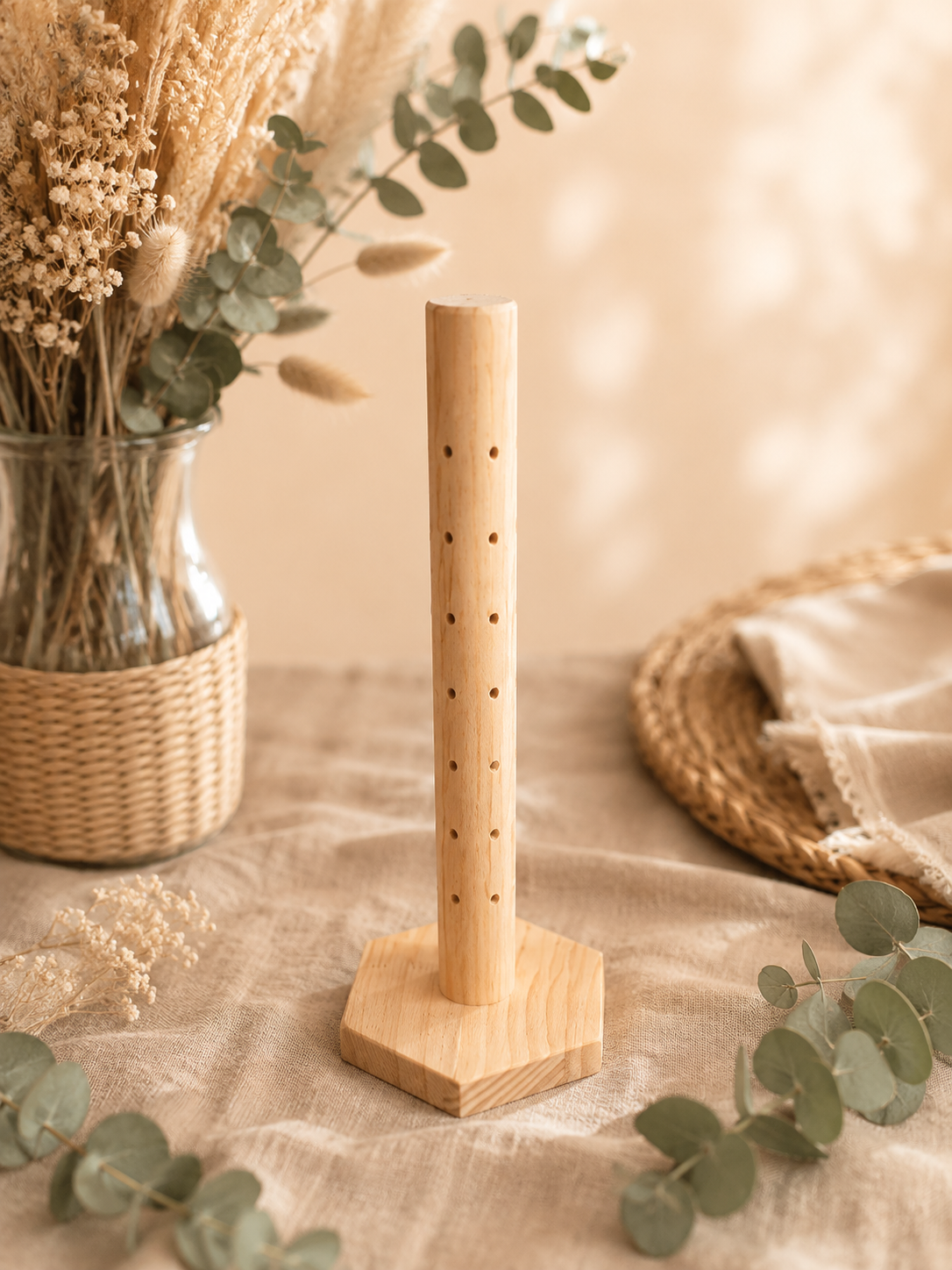 Un didgeridoo en bois posé verticalement sur une table en toile, décorée de fleurs séchées et de feuilles d'eucalyptus, avec un panier en osier contenant des fleurs séchées et un plat rond en rotin avec un torchon blanc. Ambiance chaleureuse et naturelle.
