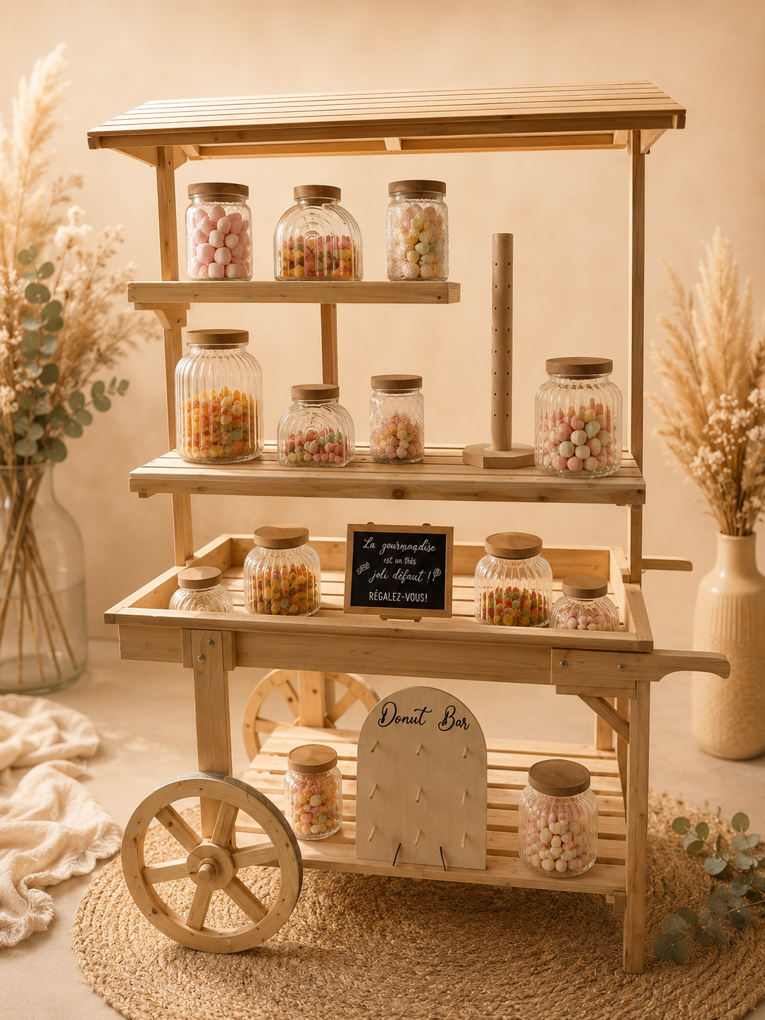 Diverse bocaux en verre remplis de bonbons colorés sur une étagère en bois, avec une petite ardoise noire indiquant un bar à donuts dans un décor chaleureux avec des fleurs séchées.