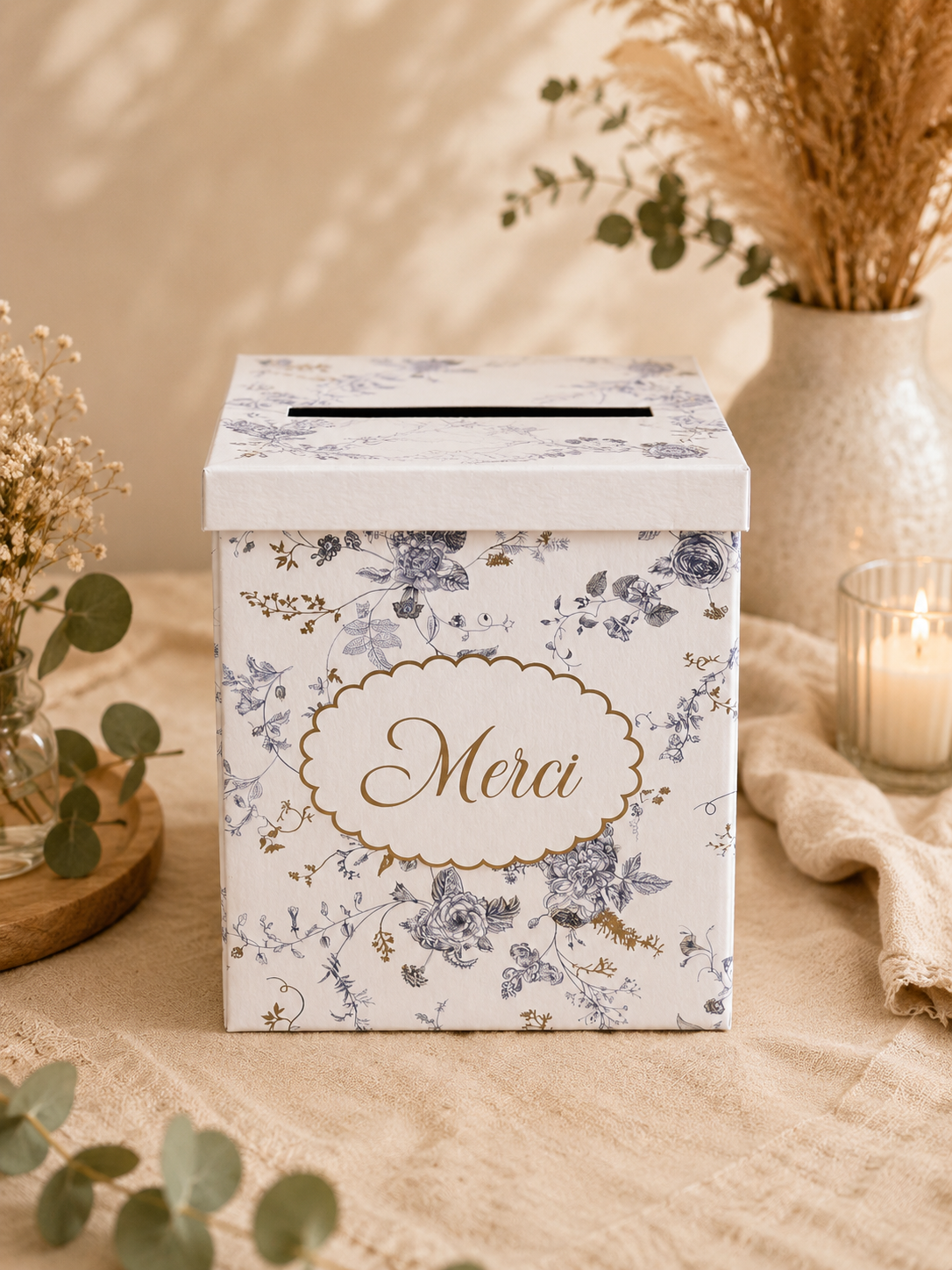 Urne blanche avec motifs floraux bleus et dorés et inscription « Merci » en location pour mariage, baptême, communion ou anniversaire. Une urne raffinée pour recueillir les enveloppes de vos invités. Disponible chez Les Jolis Instants.