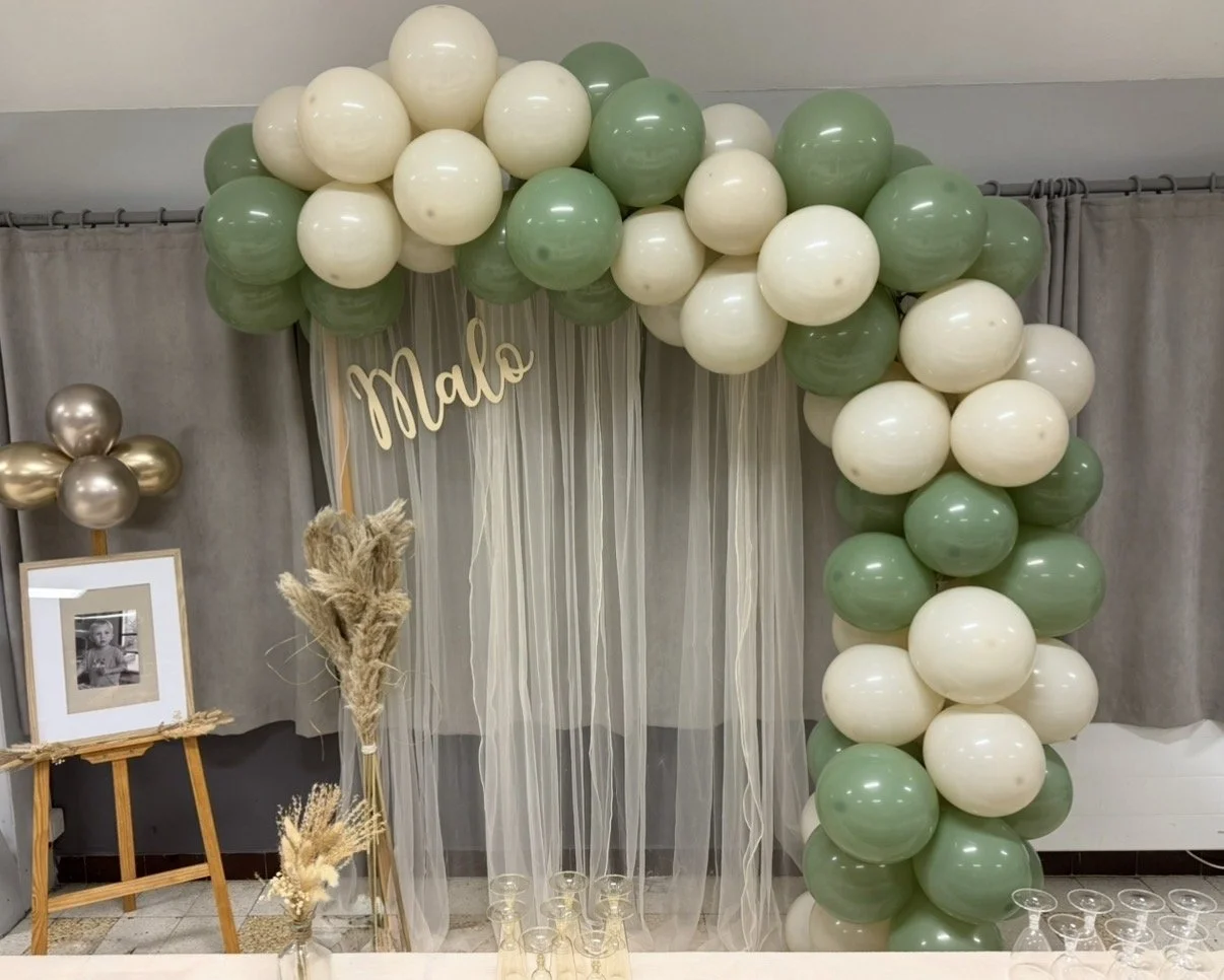 Décoration de baptême avec arche organique de ballons vert sauge, blanc et beige, toile de fond et prénom personnalisé en bois  “Malo”, chevalet en bois et coin photo pour baptême.