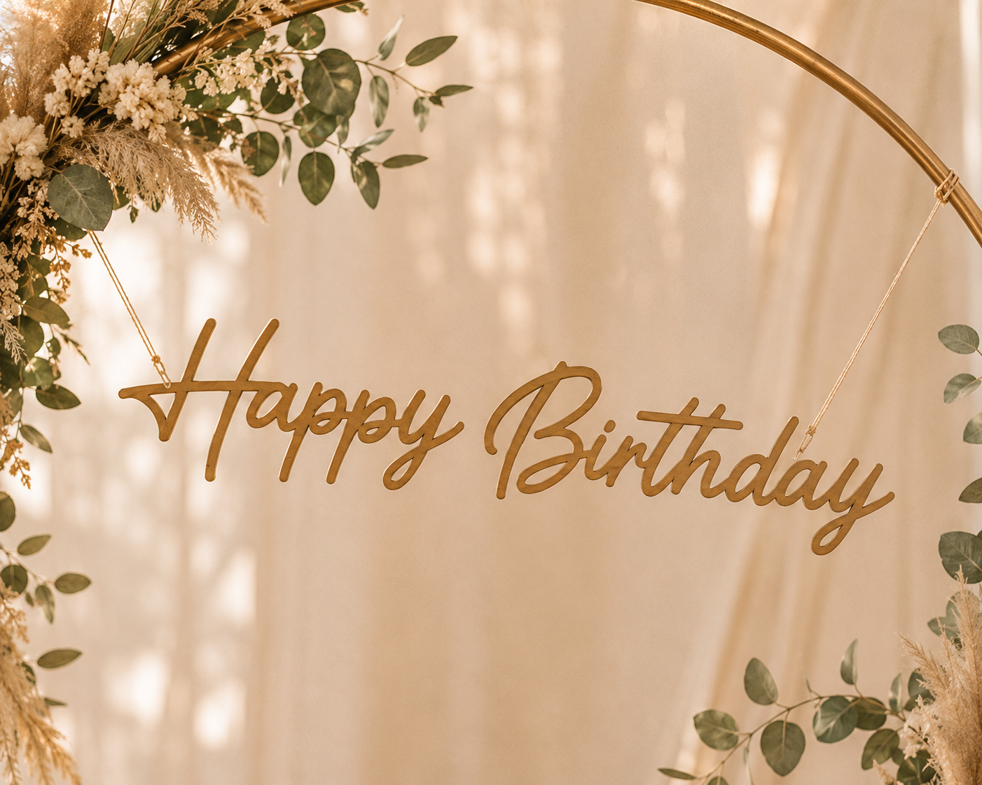 Une décoration florale avec un message en bois 'Happy Birthday' suspendu, entourée de feuillage vert et de fleurs séchées, sur un fond clair.