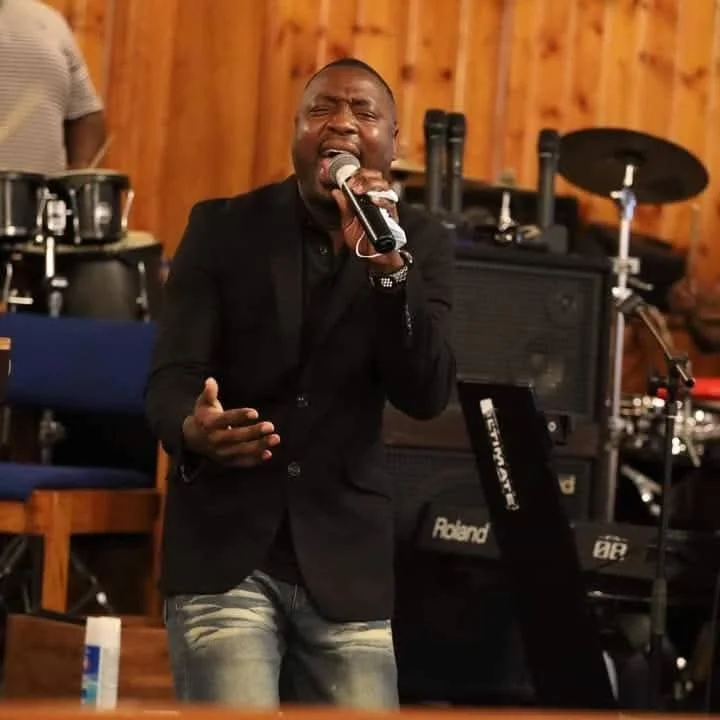 Man singing passionately into a microphone during a musical performance in a wooden-paneled room.