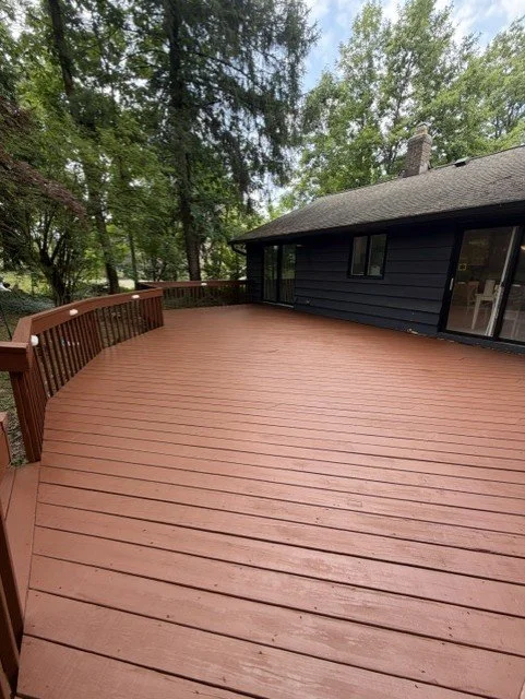 Large wooden deck attached to a house, surrounded by trees.