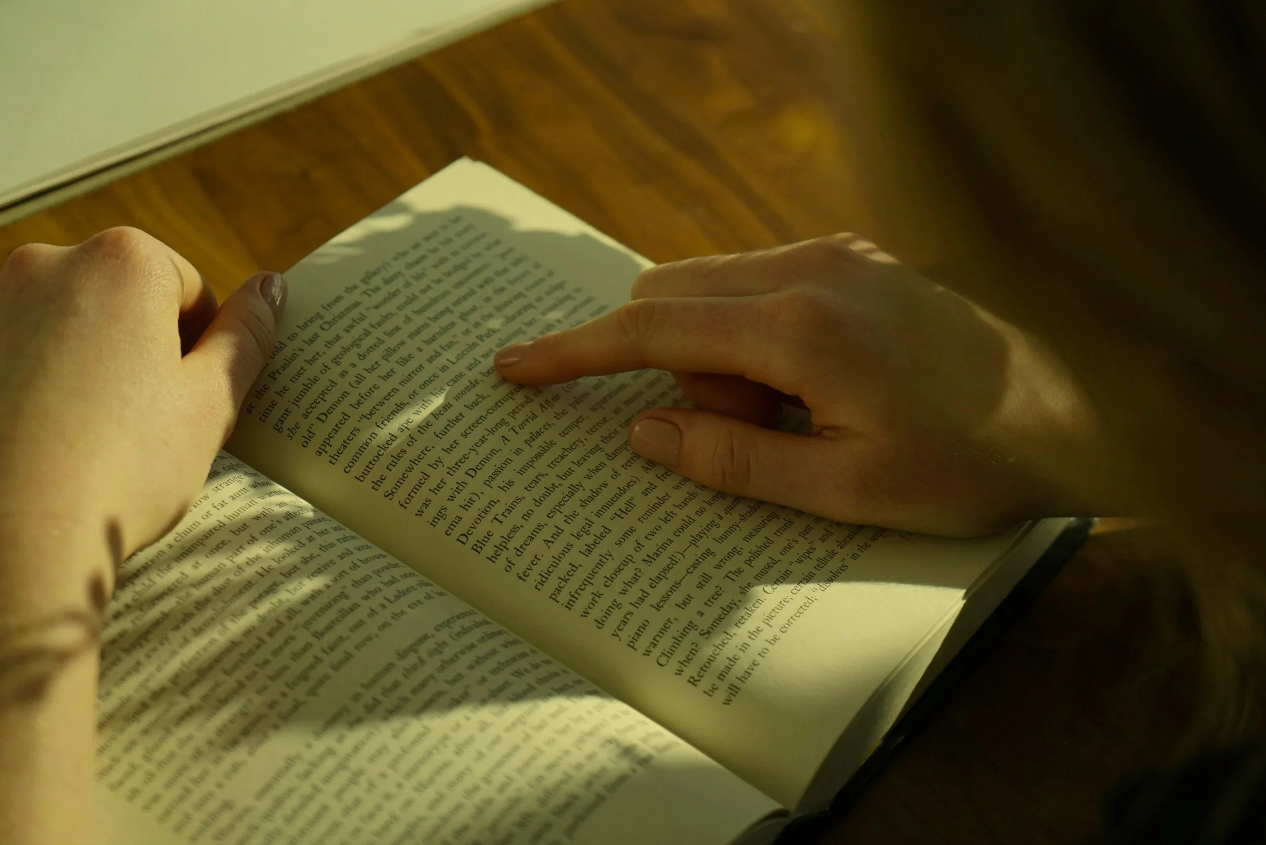 Close-up of a person's hands holding a book while reading on a wooden surface.