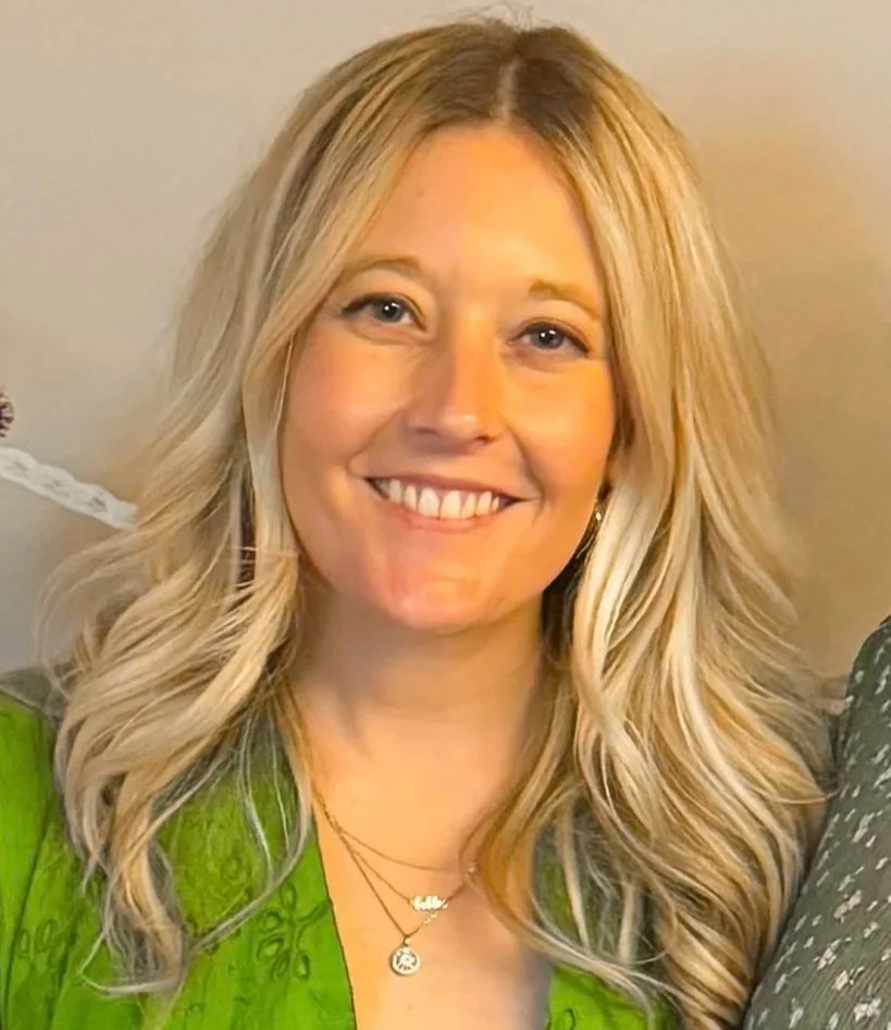 A woman with long blonde hair wearing a green top and layered necklaces smiling at the camera.