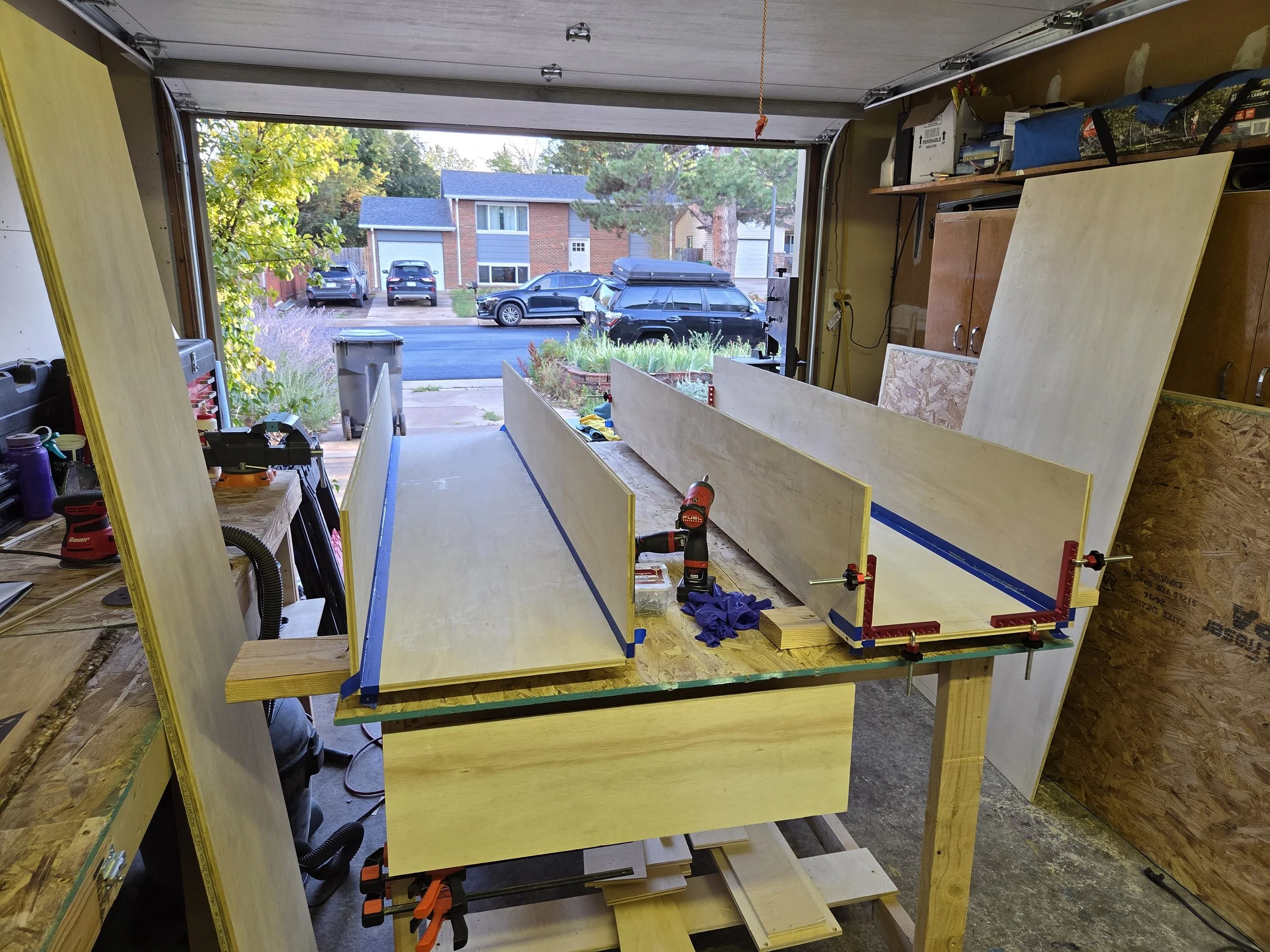 View of a residential neighborhood through an open garage door, with parked cars and houses in the background, taken from inside a garage under construction.