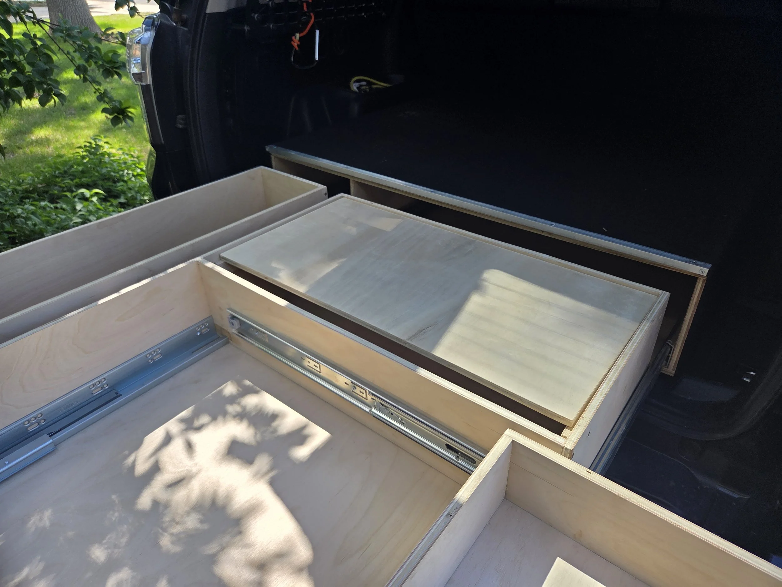 Unassembled light-colored wooden drawers or cabinets inside a black trailer or vehicle, with some cables visible.
