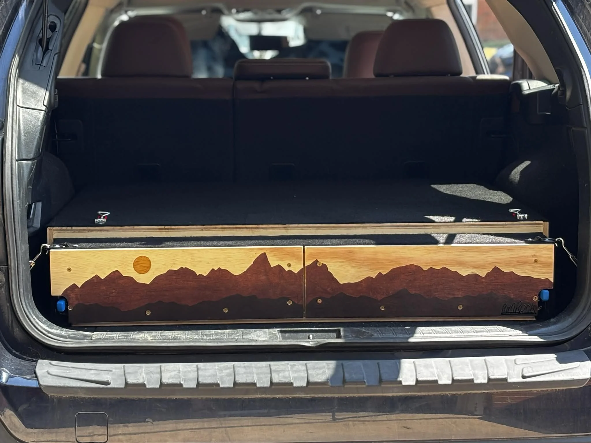 The back of an SUV with the trunk open, revealing a painted mountain scene on the inside of the trunk door.