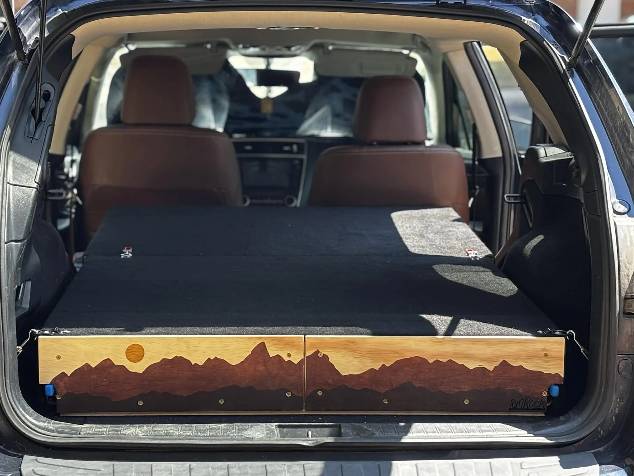 The interior of a vehicle with brown seats and a wooden decorative panel at the rear, featuring a mountain landscape scene.