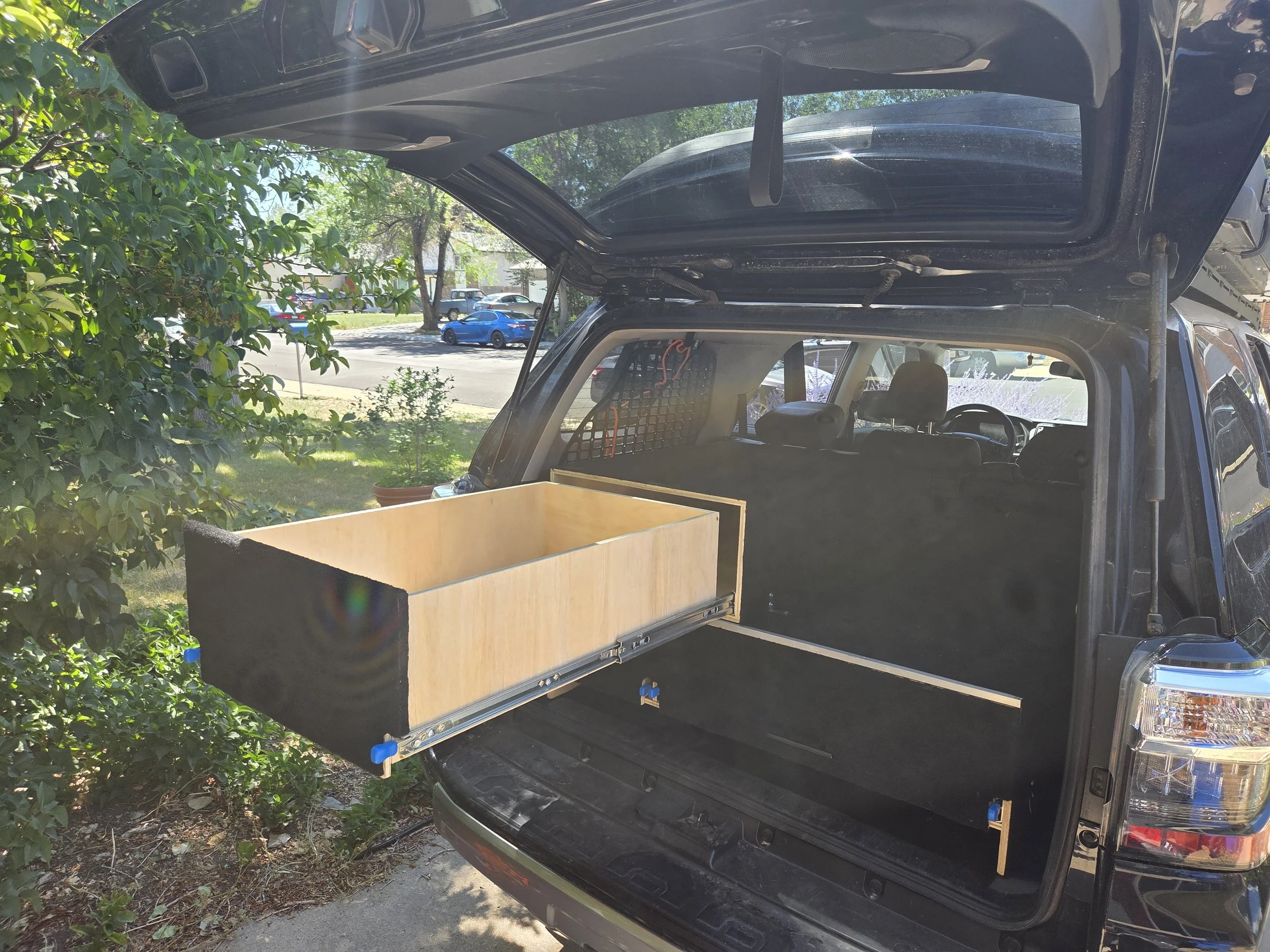 The back of an SUV with an open tailgate, showing a large wooden drawer slide installed inside.