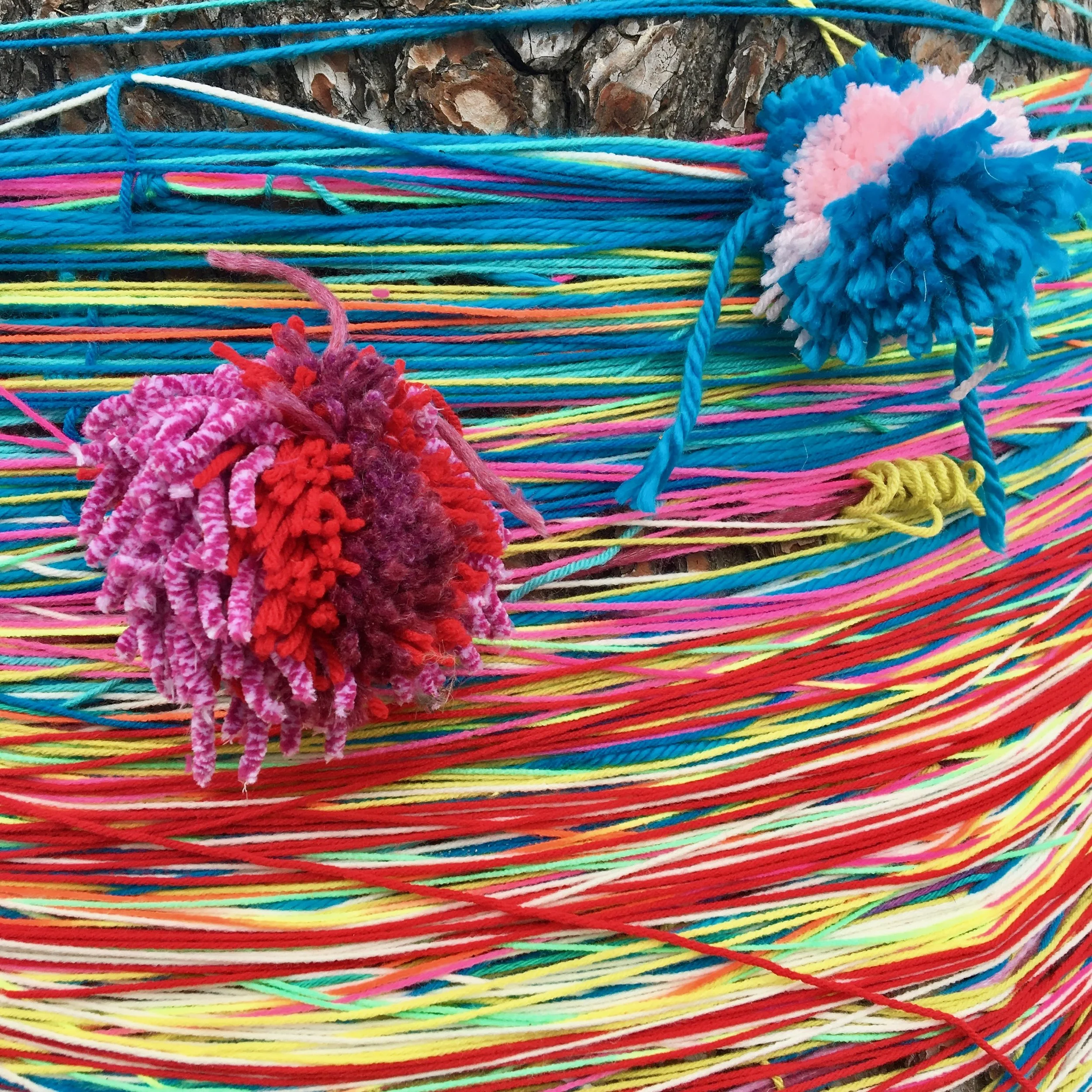 Close-up of colorful yarn and knitting pom-poms on a tree bark background.