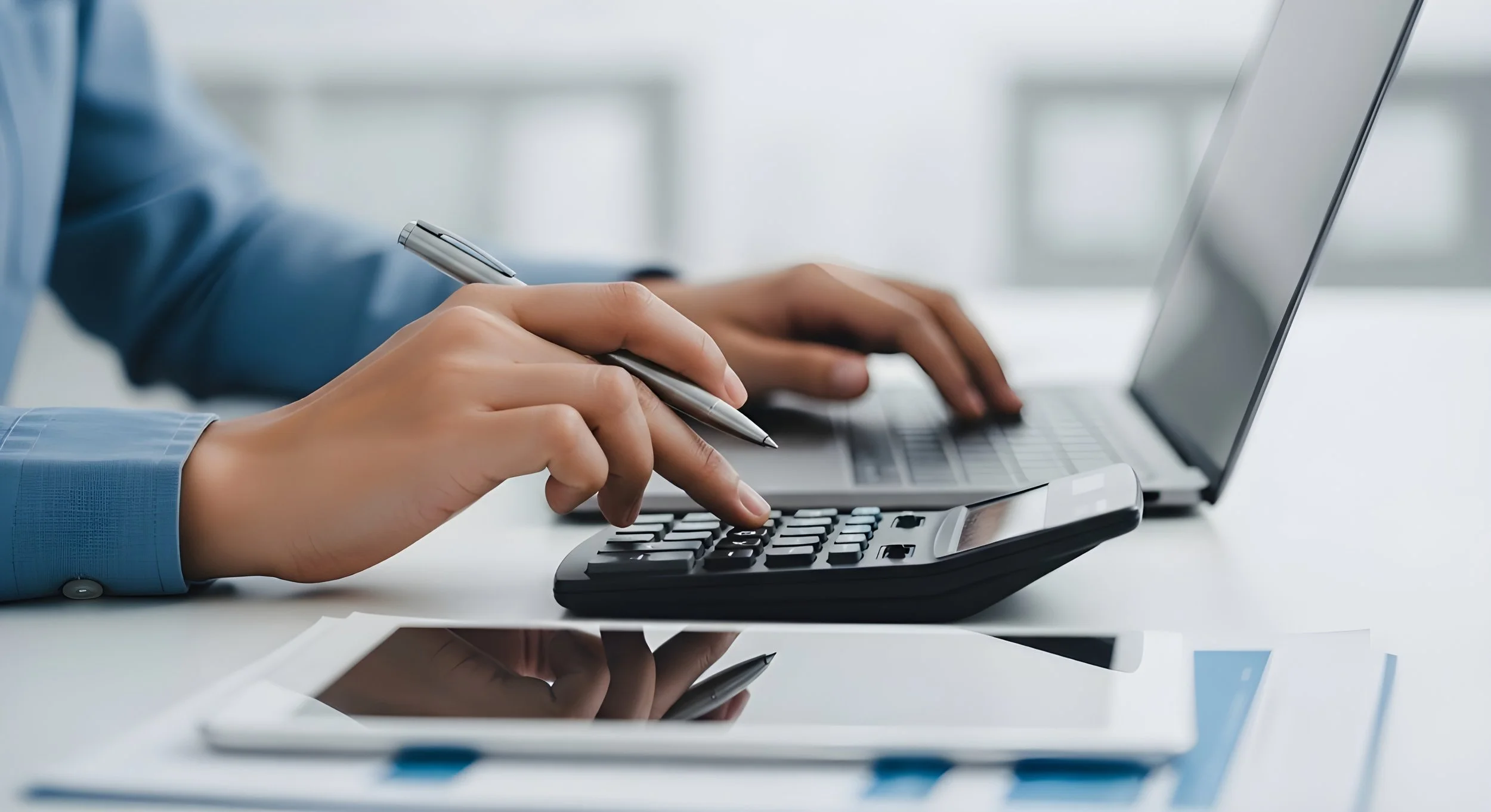 Persona usando una calculadora y un teléfono móvil en un escritorio de oficina.