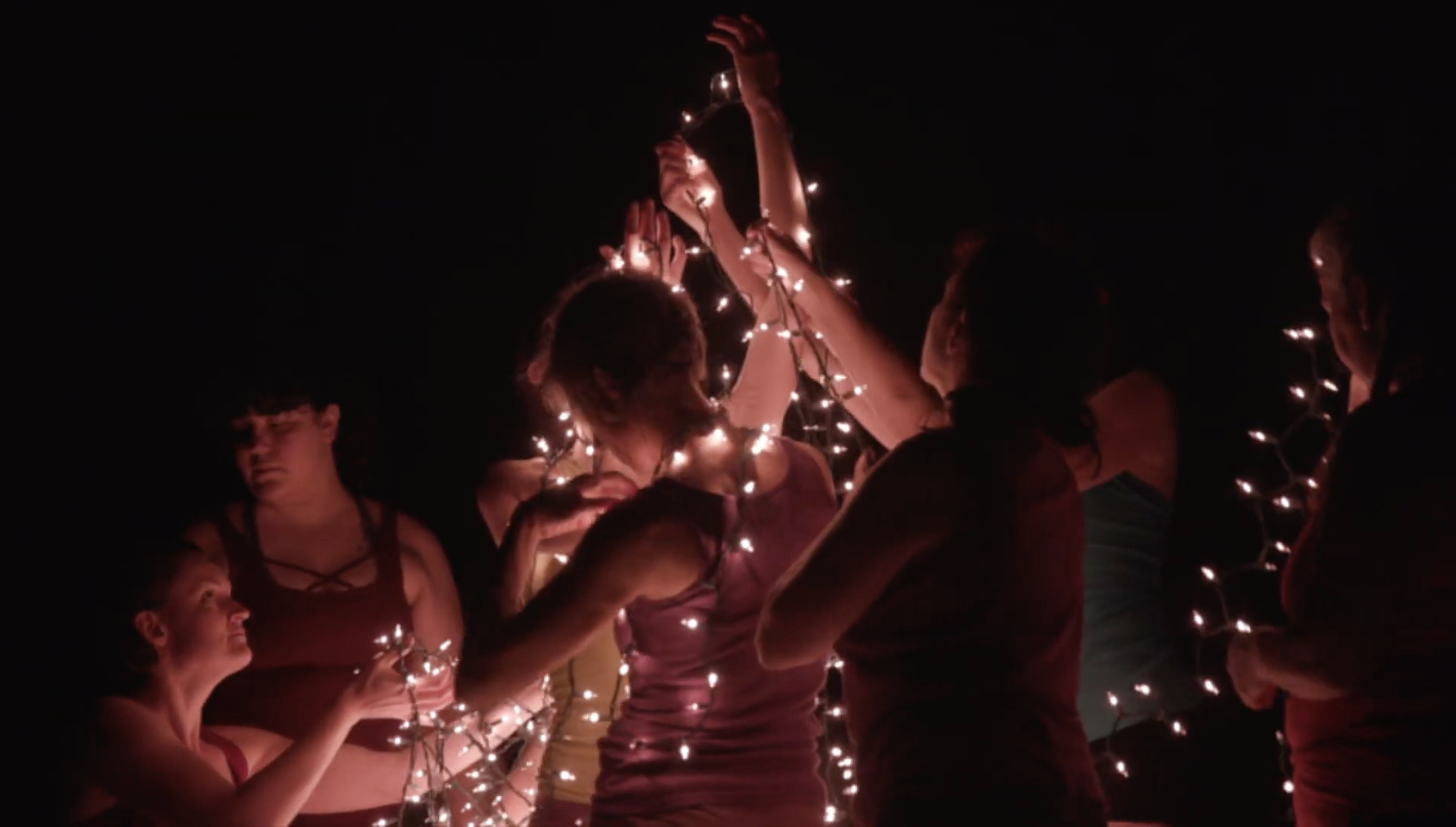 Dancers holding and wrapped in string lights during a night performance at the Phantom Theater in Warren, Vermont.
