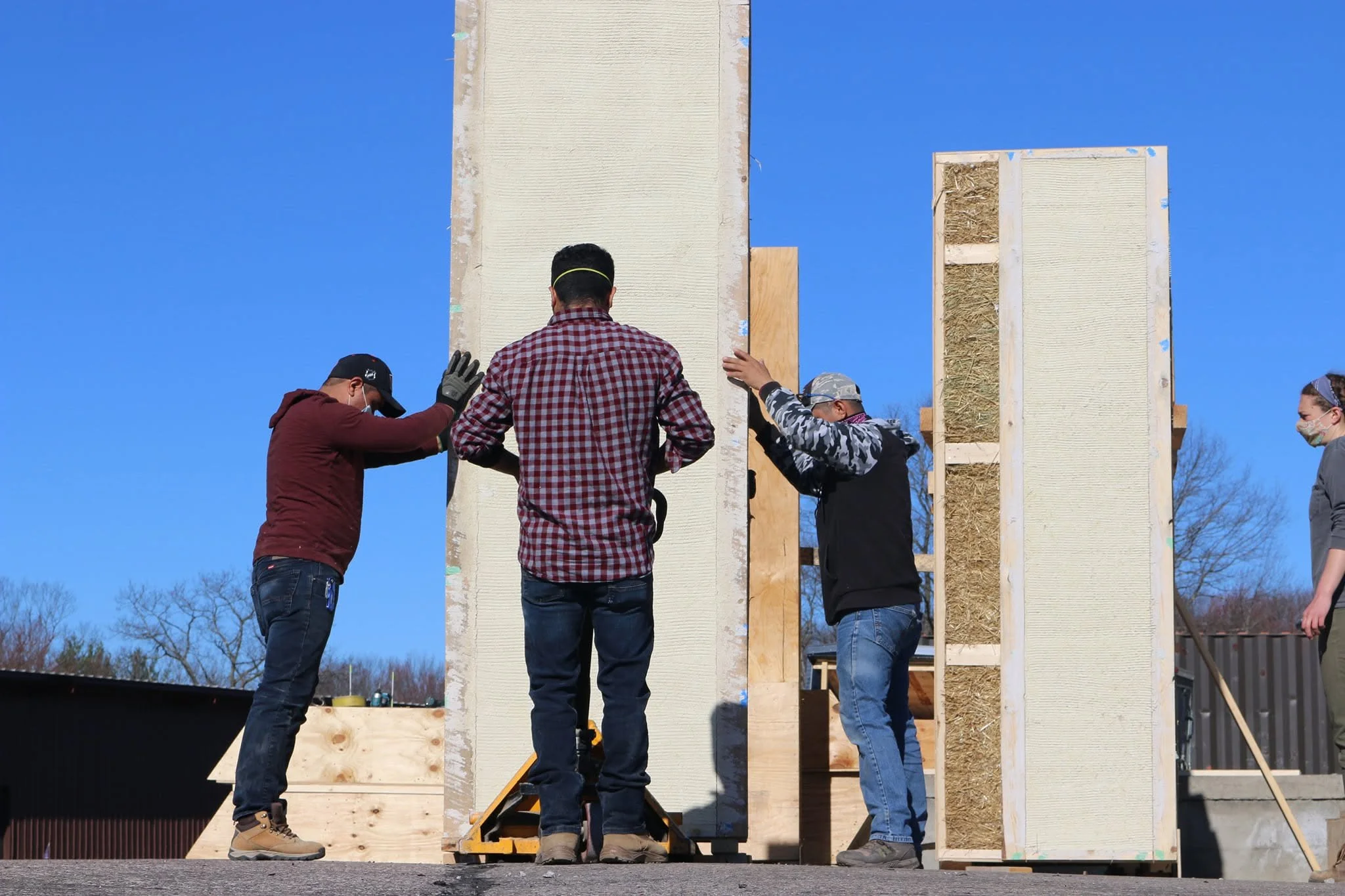 People working on a building construction, assembling wooden frame walls outdoors on a sunny day.
