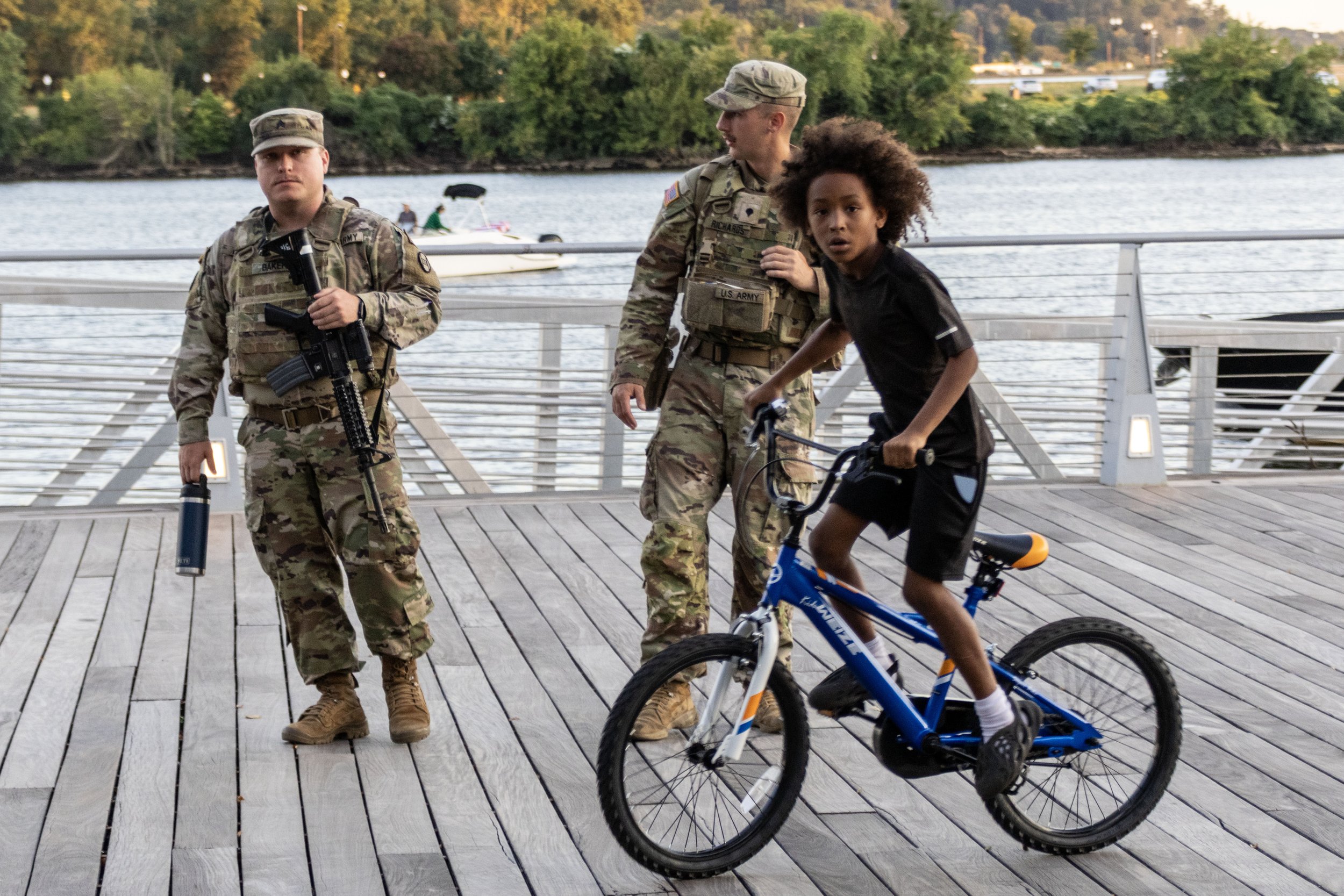 Kid biking past the National Guard in Navy Yard - August 31, 2025