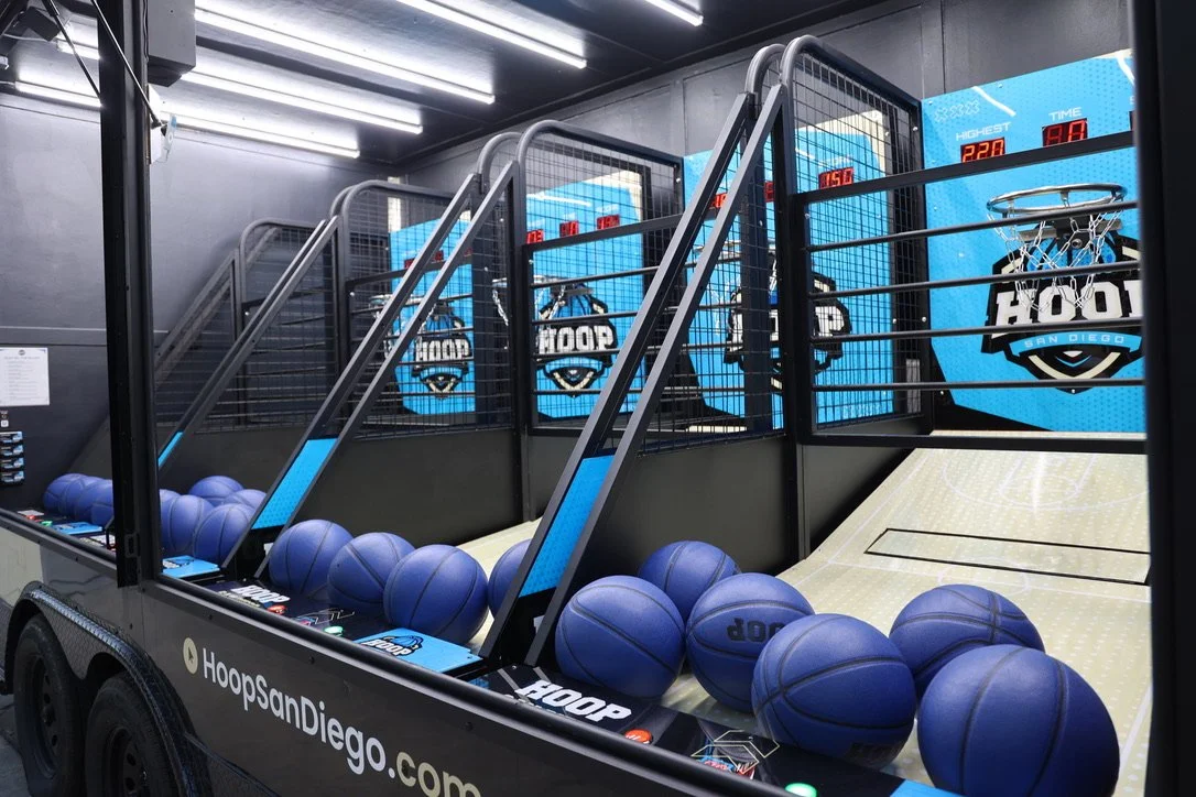 Basketball arcade game with blue basketballs, digital scoreboard, and Hoop San Diego logo in the background.