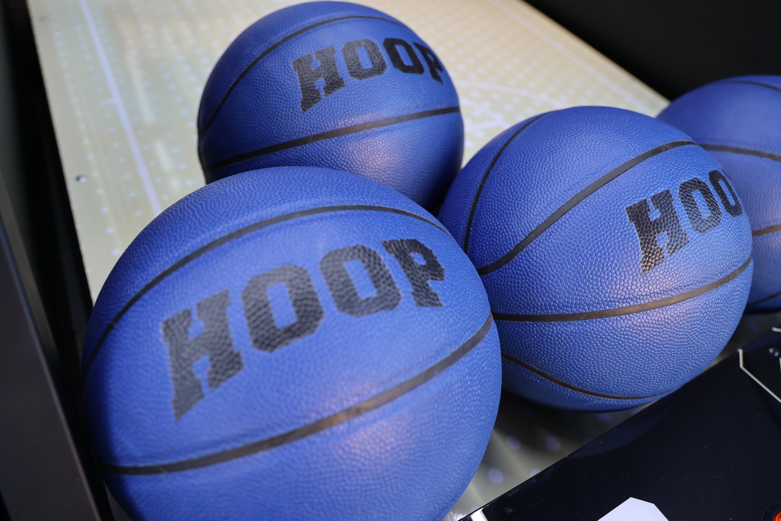 Close-up of multiple blue basketballs with black lines and the word 'HOOP' printed on them, arranged in a container or car.