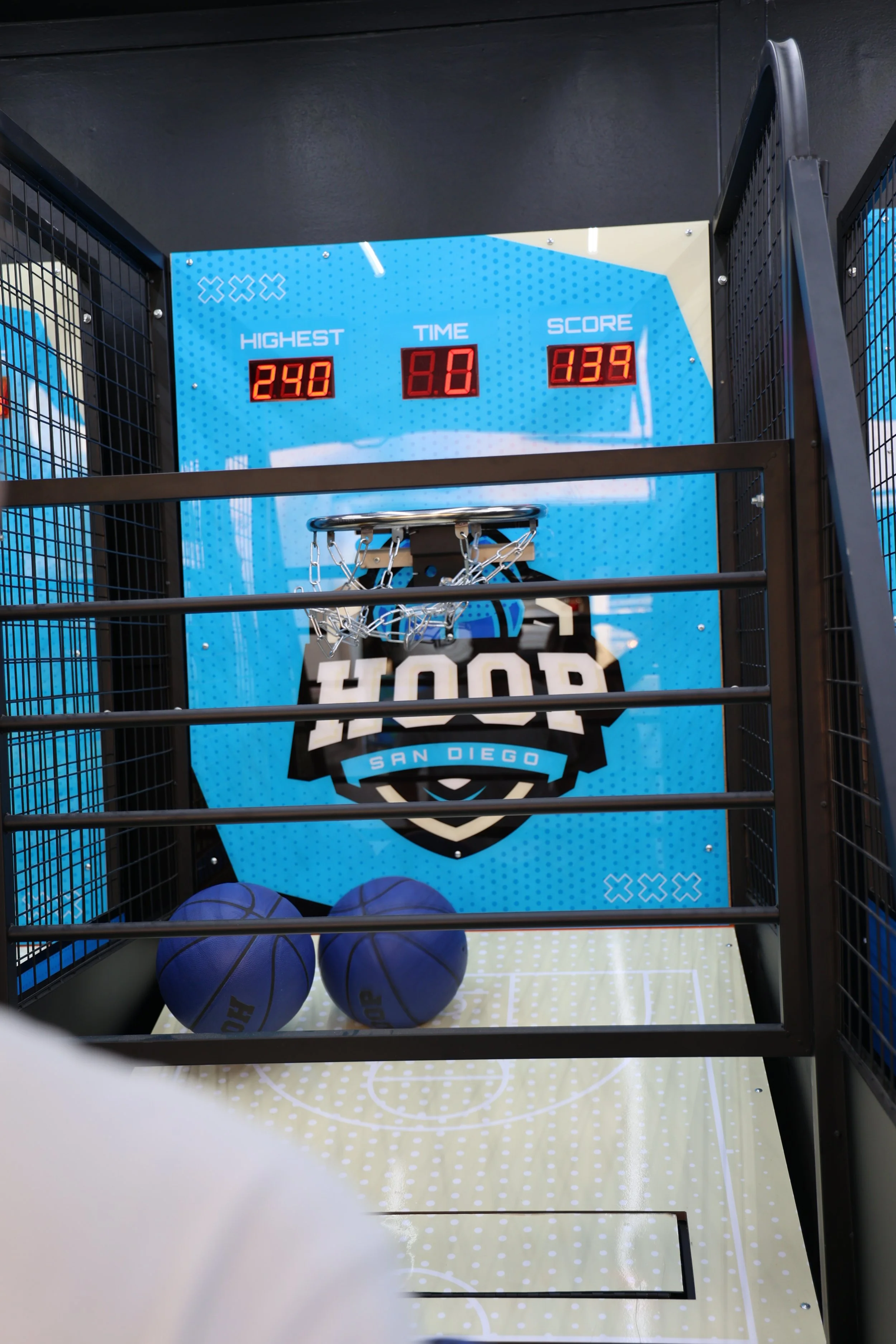 A basketball arcade game with digital score display, three purple basketballs on the floor, and the words 'STOP' and 'San Diego' on the backdrop.