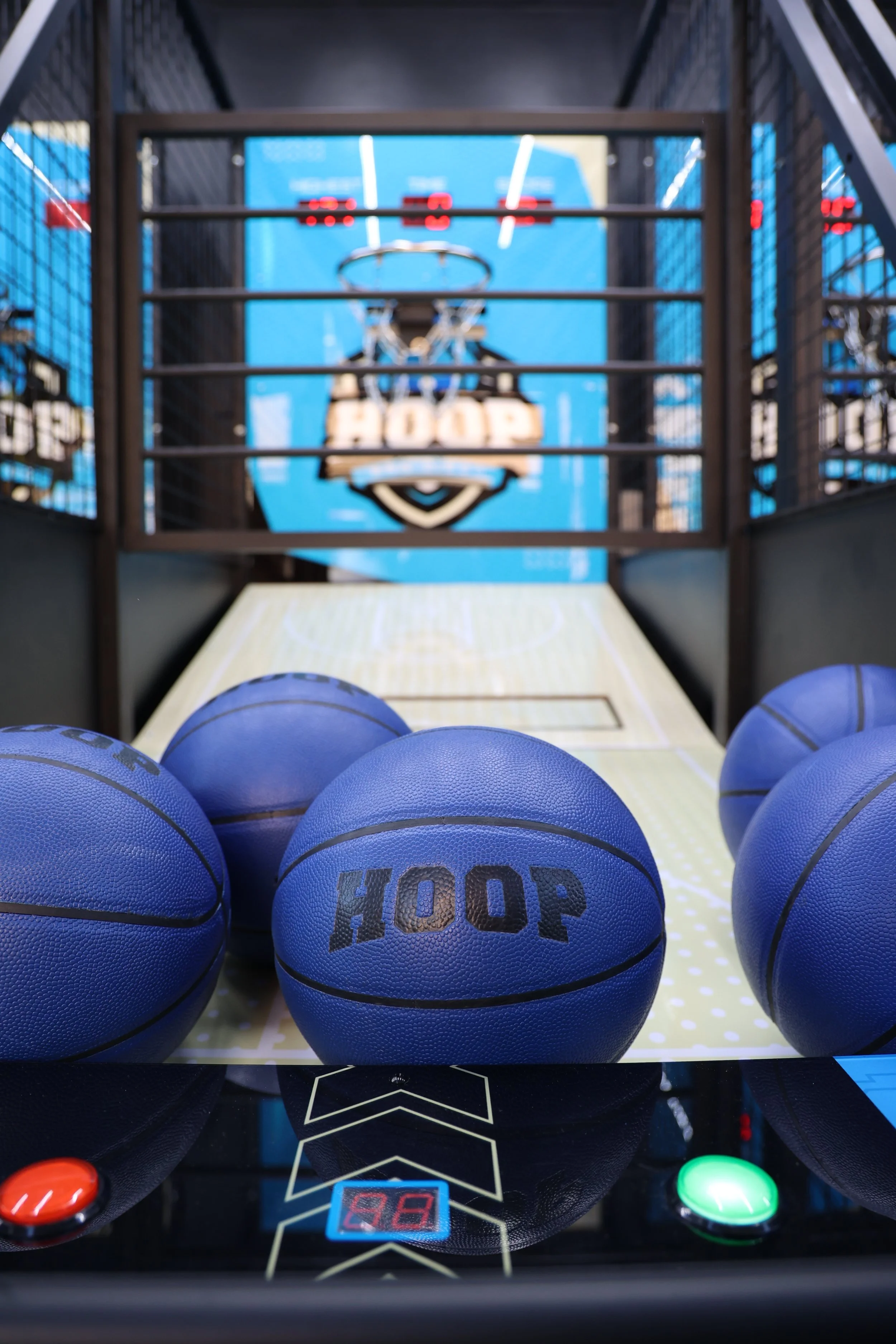 An air hockey table with blue hockey pucks labeled 'HOOP'. The table has digital score displays showing the number 98, with red and green control buttons at the corners. There are basketball hoops above the score displays.