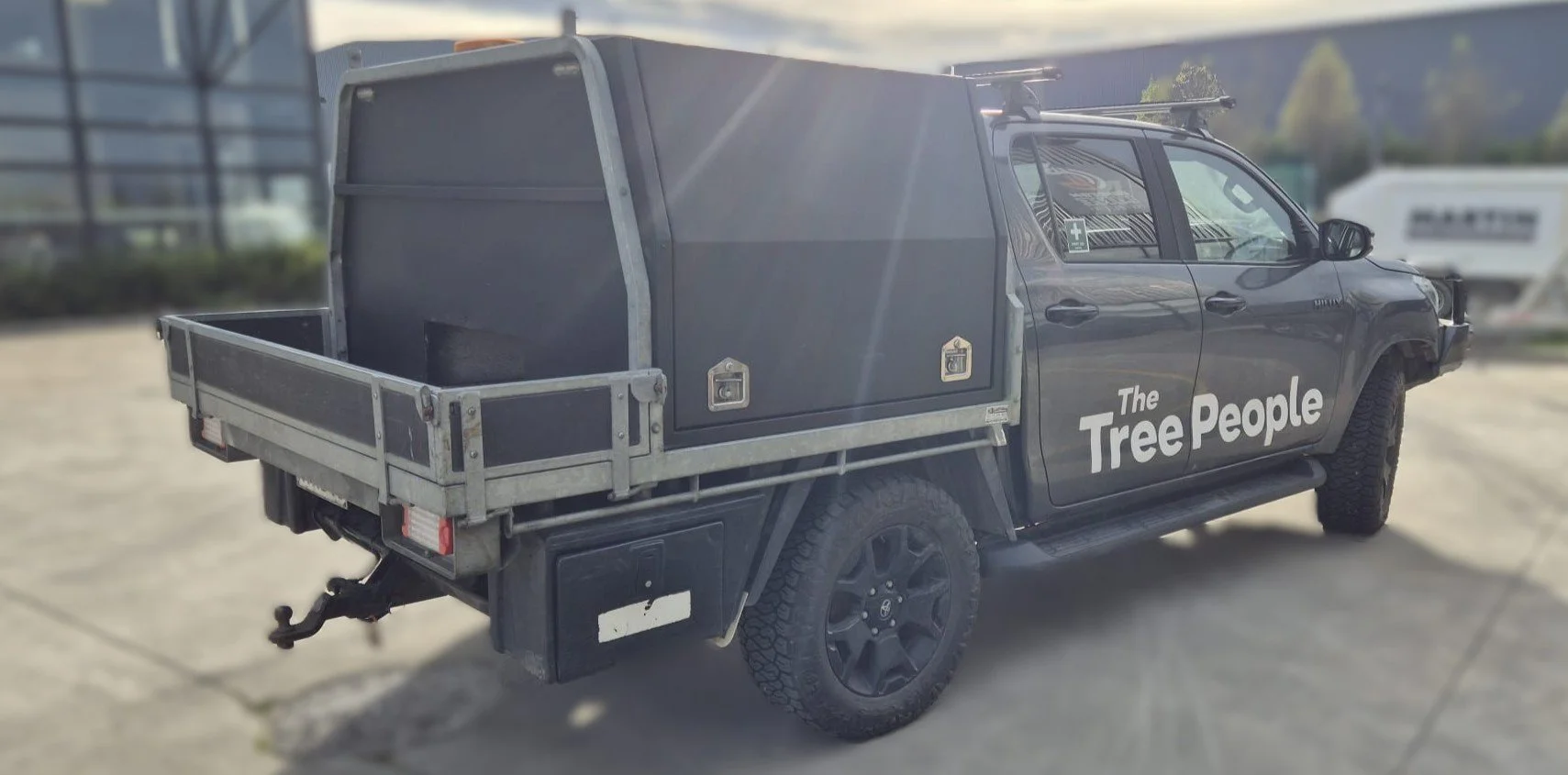 A black ute with a storage box on the back, with lockable doors marked with 'The Tree People'' logo.