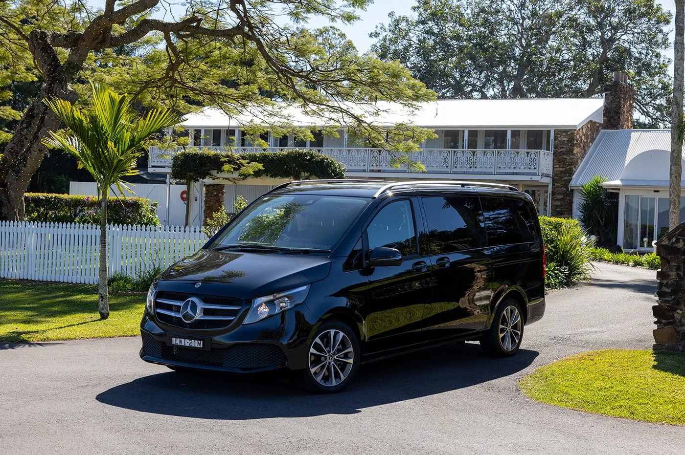 Black Mercedes-Benz van parked on a driveway in front of a house with a white picket fence and lush greenery.