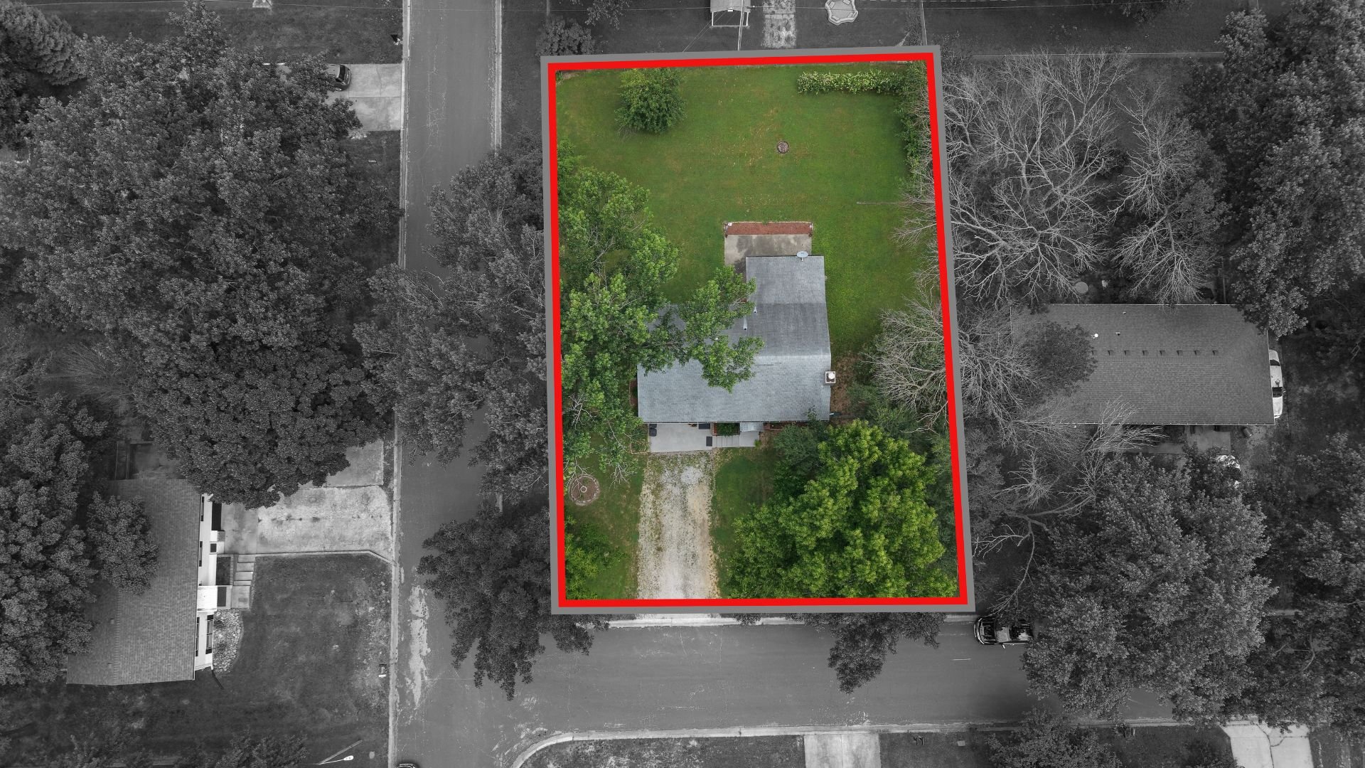 Aerial view of a residential backyard with a house, surrounded by tall trees and a lawn, enclosed by a red border.