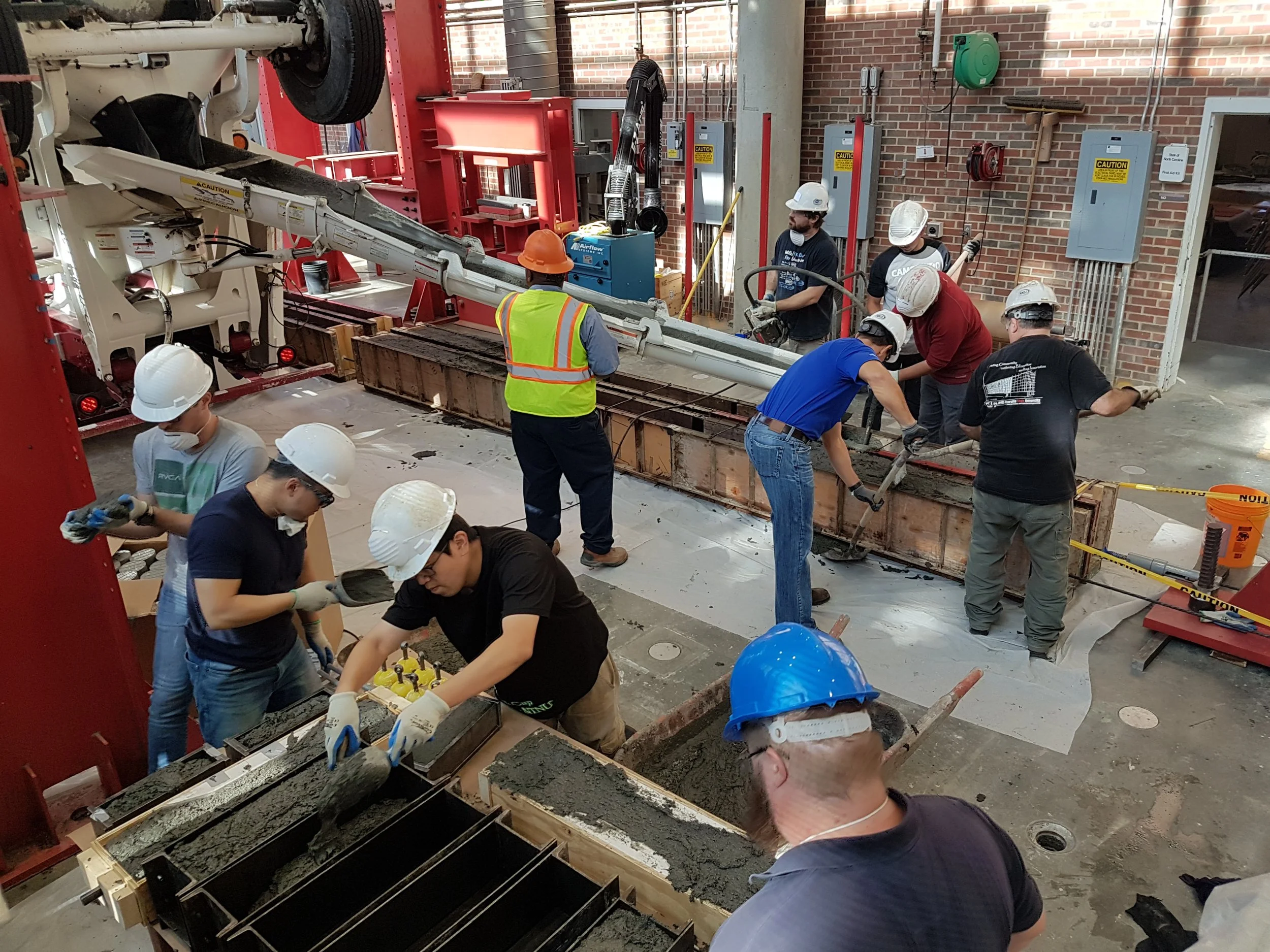 Personas trabajando en construcción de concreto con maquinaria y herramientas en un espacio cerrado con paredes de ladrillo y equipo de seguridad