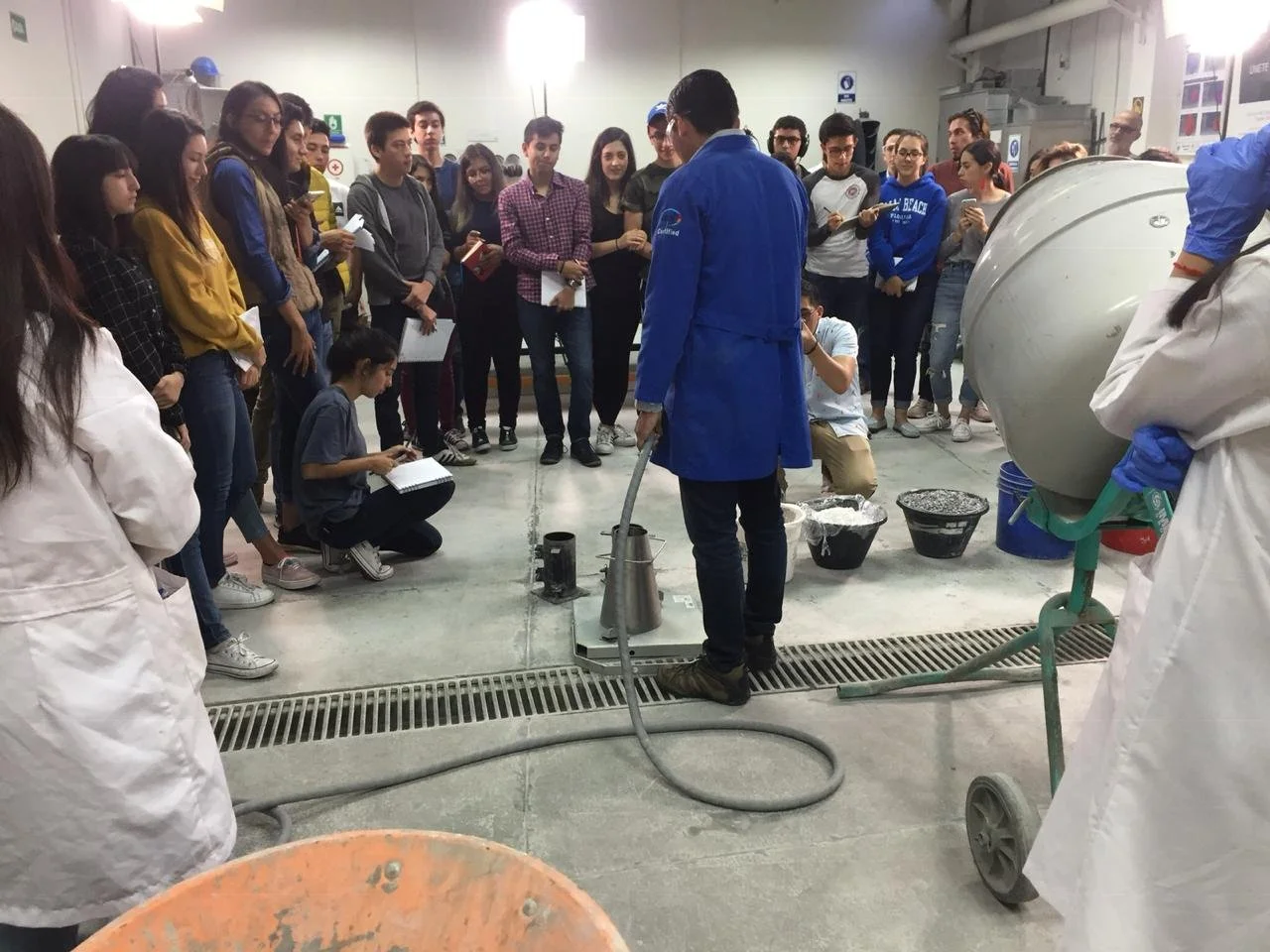 Grupo de estudiantes y profesores en una demostración de laboratorio con un especialista usando equipo de protección en un aula de ciencias.