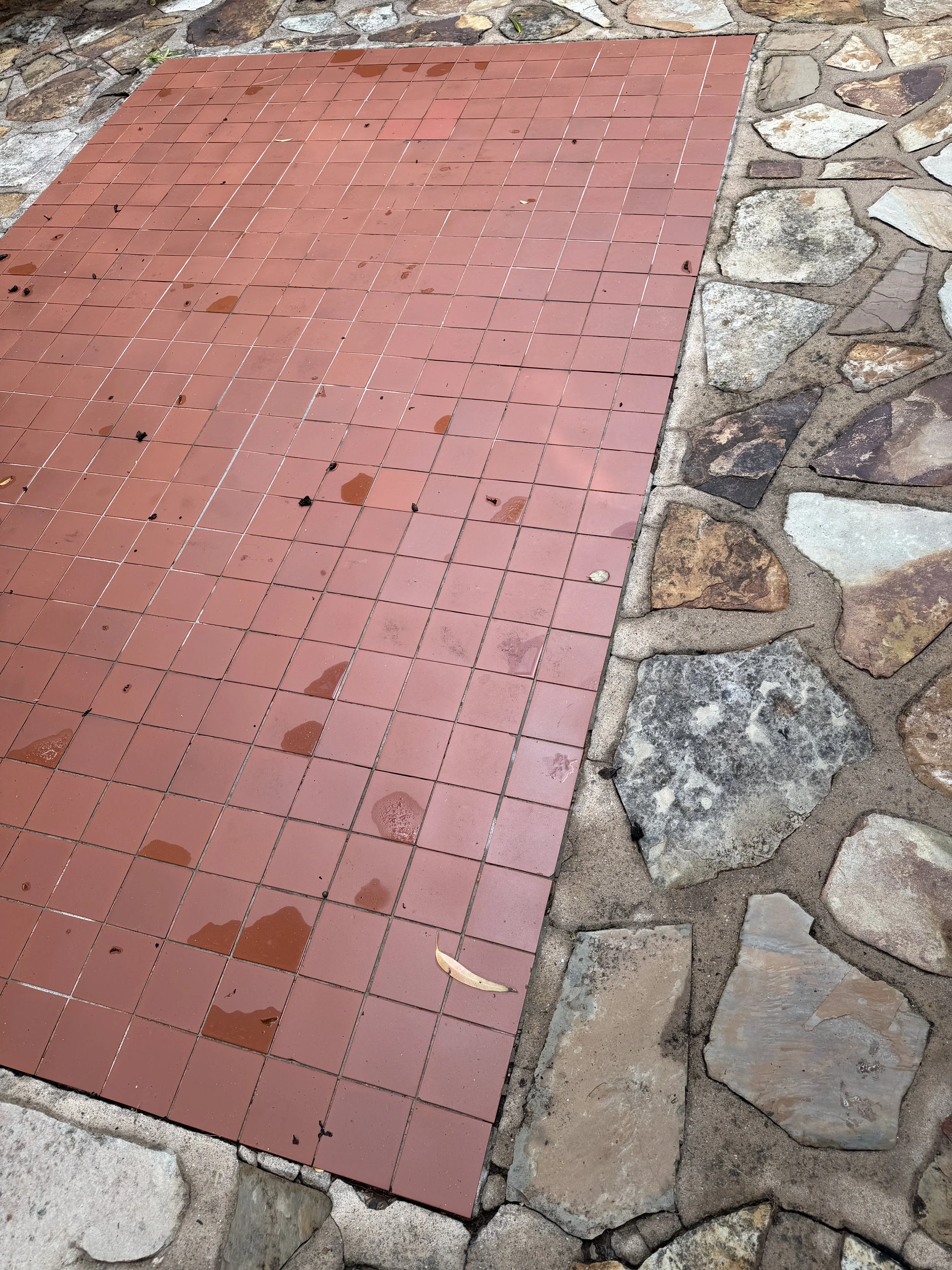 A section of a paving just cleaned showing a transition from stone paving on the right to a newly installed red tile section on the left.