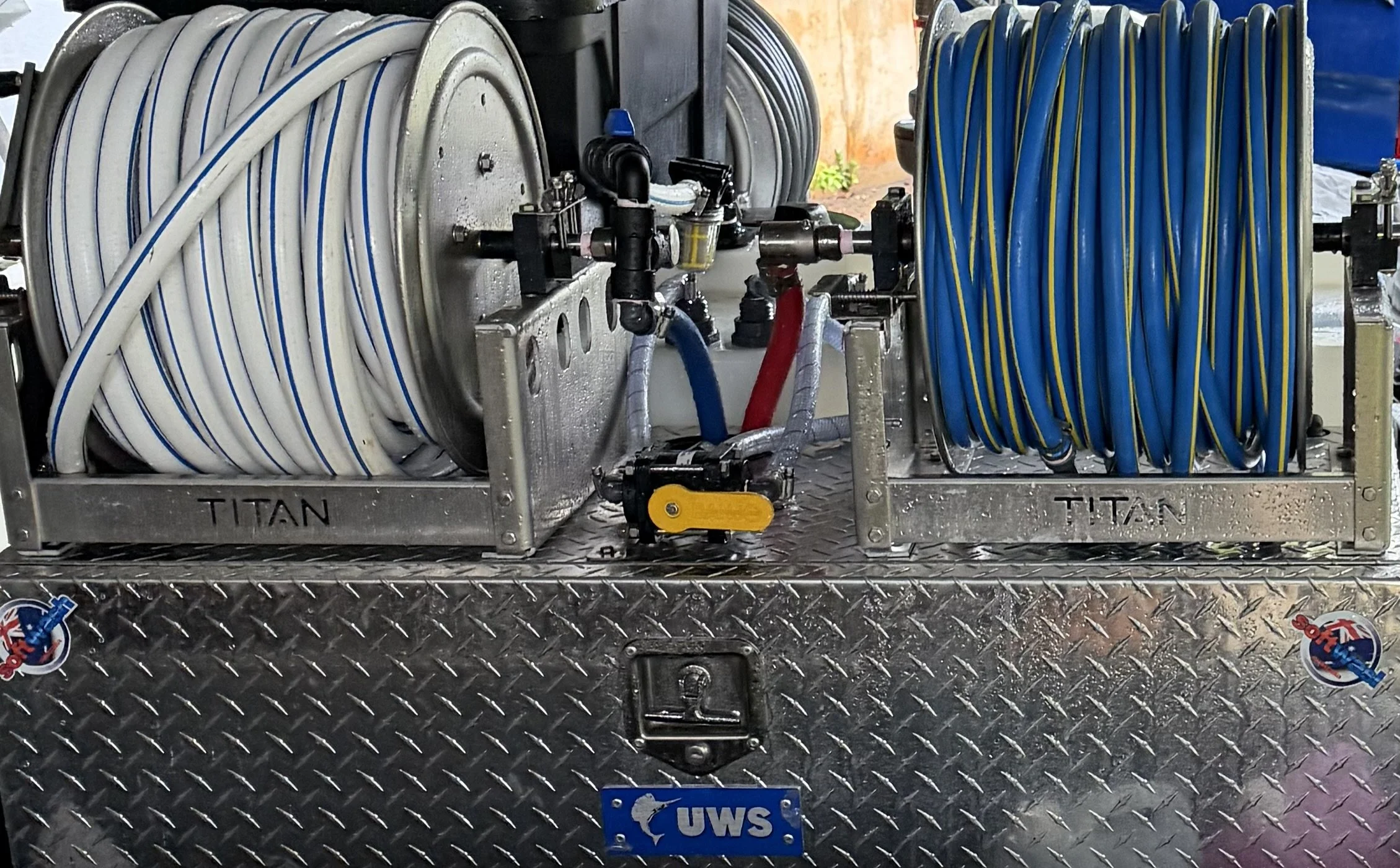 A fire truck equipment panel with hoses in white and blue, mounted on a metal surface with diamond plate texture, and UWS logo at the bottom.