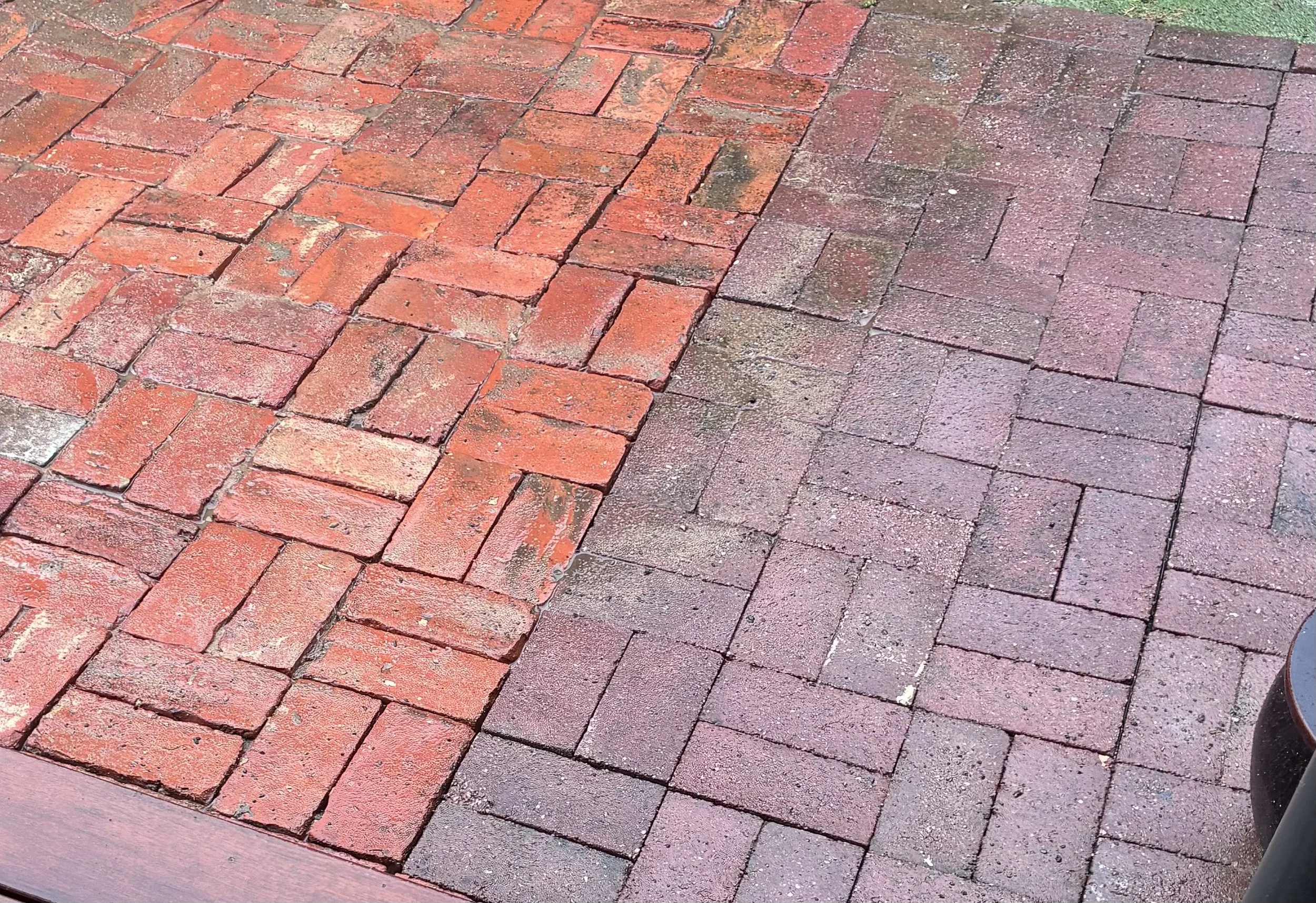Red brick patio with some black dirt and moss, and part of a dark gray planter or container on the right side.
