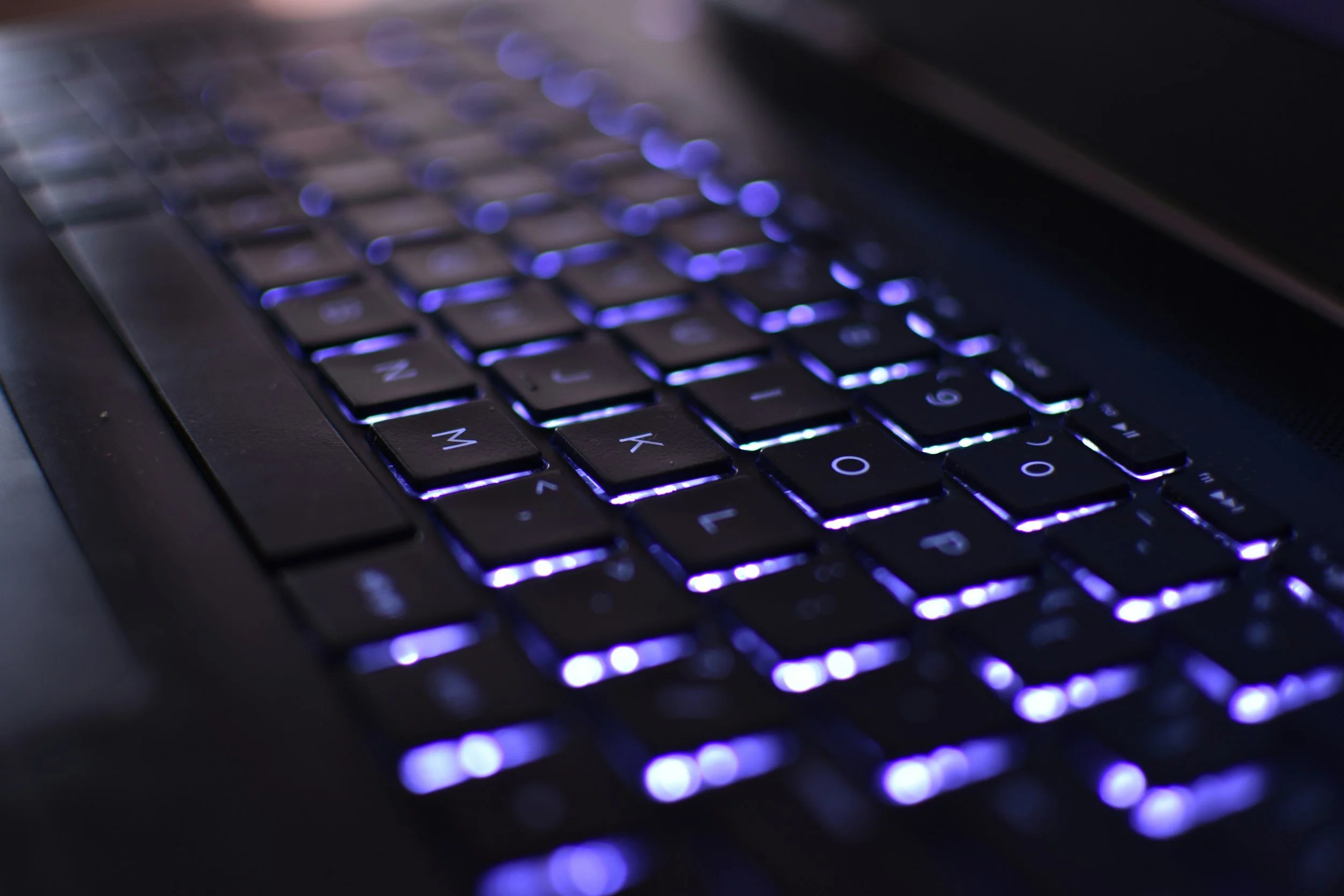 Close-up of a laptop keyboard with purple backlit keys, showing some keys with visible letters and symbols.