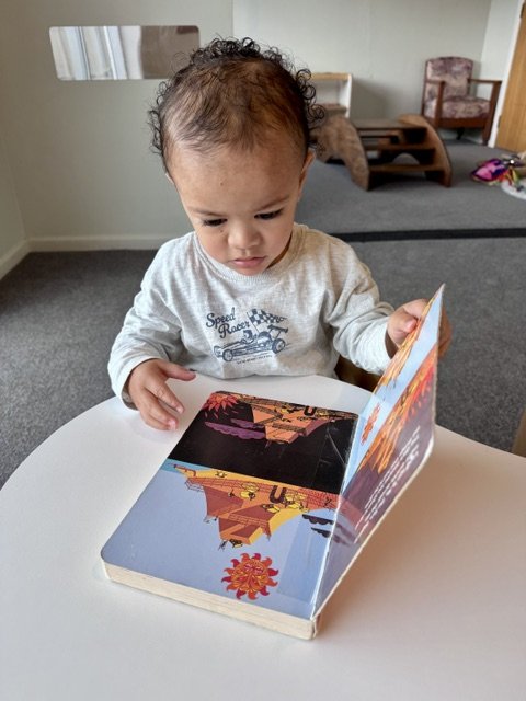 Child exploring books independently, fostering early literacy, language development and a love of reading.