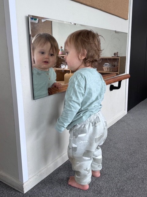 Toddler exploring their reflection, developing self-awareness, curiosity and confidence through independent exploration.