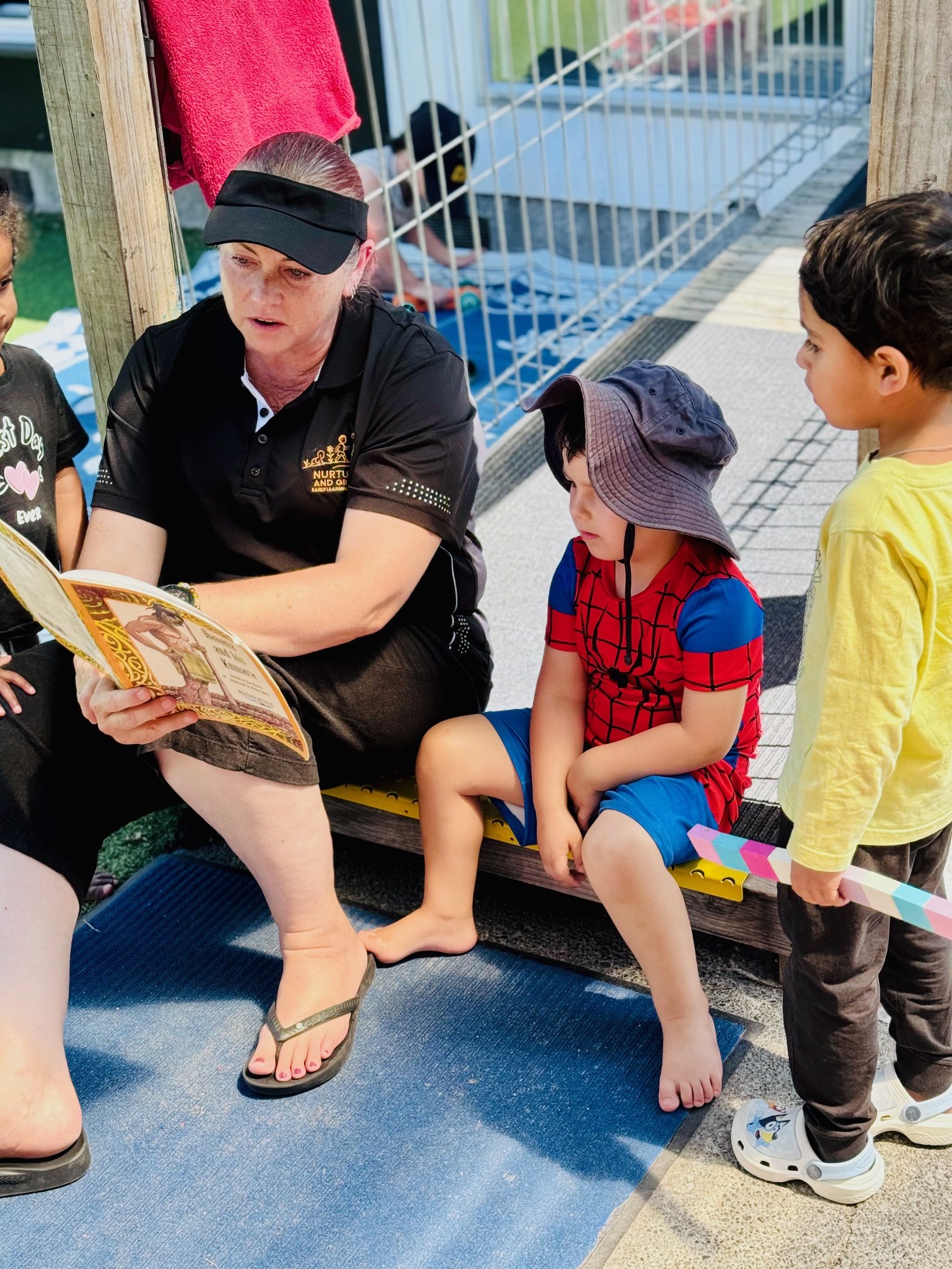 Teacher sharing stories outdoors, fostering early literacy, language development and a love of reading in a calm learning environment.