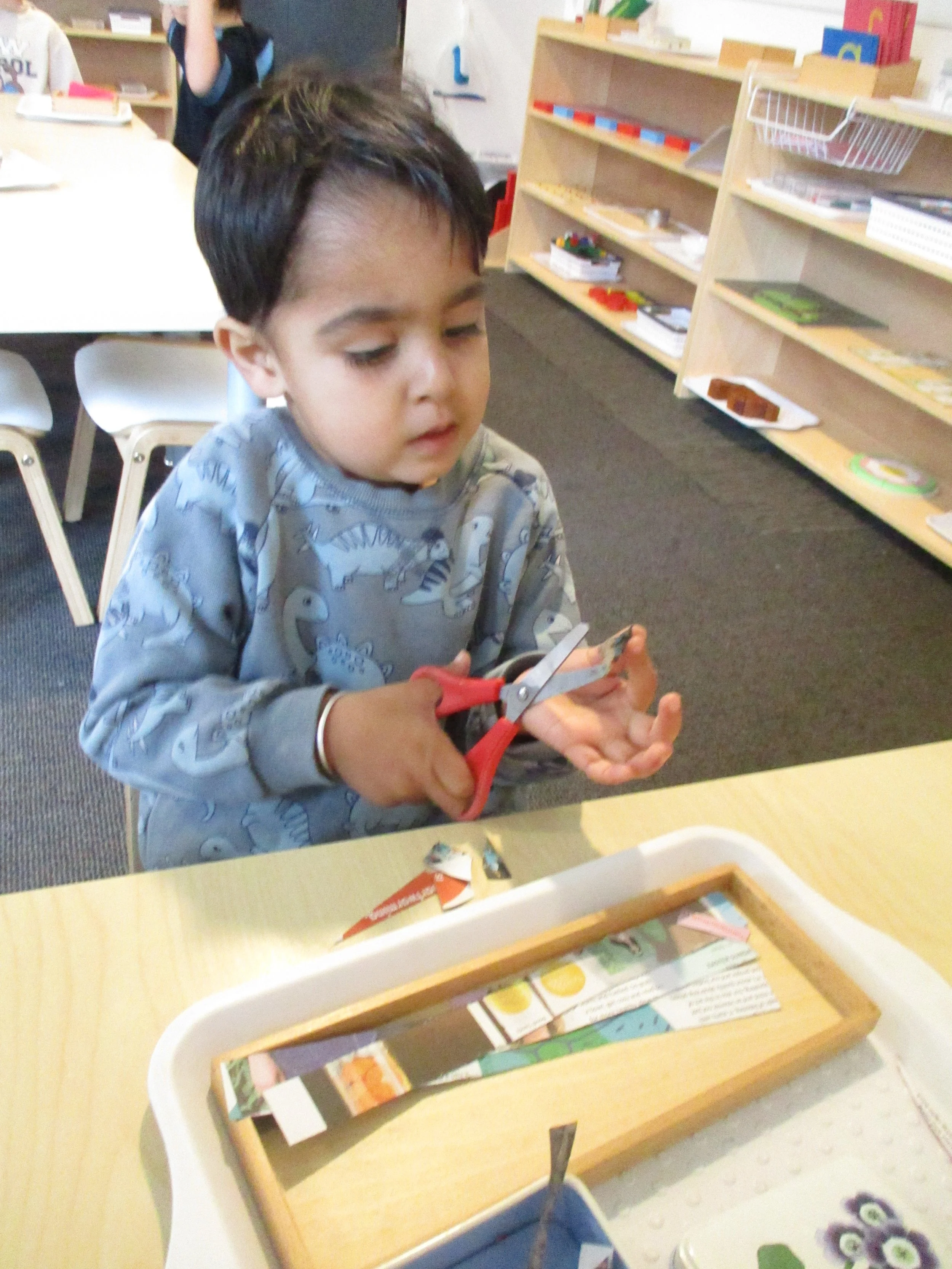 Child strengthening fine motor skills and hand control through cutting activities, supporting independence, creativity and early writing development.