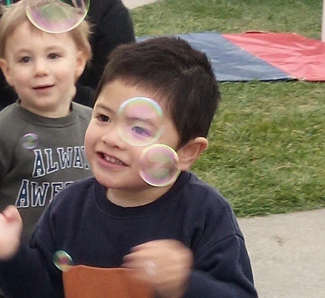 Children enjoying bubble play outdoors, developing coordination, communication and joyful social interactions through active play.