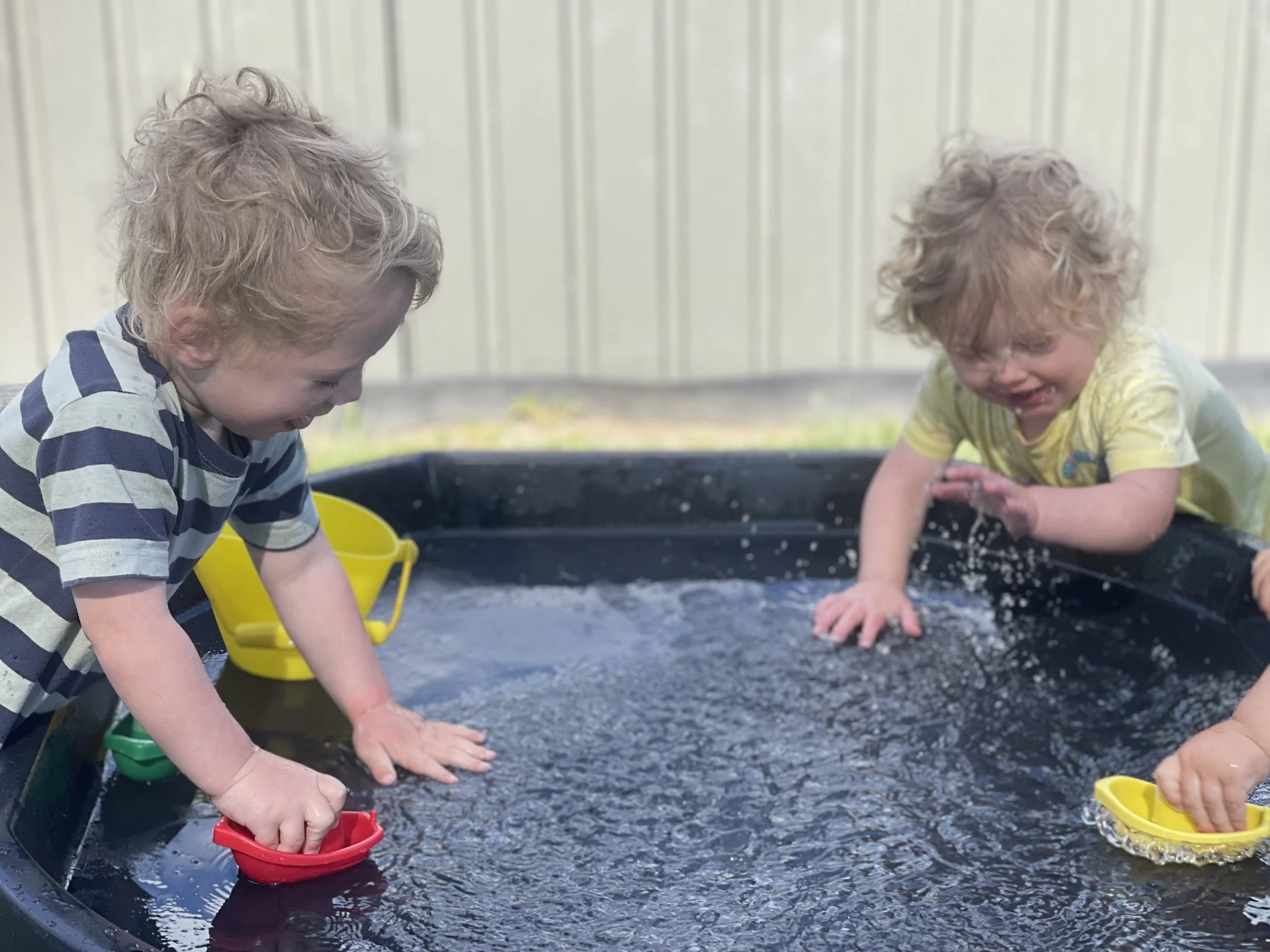 Children exploring water, pebbles and natural materials, encouraging curiosity, sensory exploration and early scientific thinking through hands-on play.