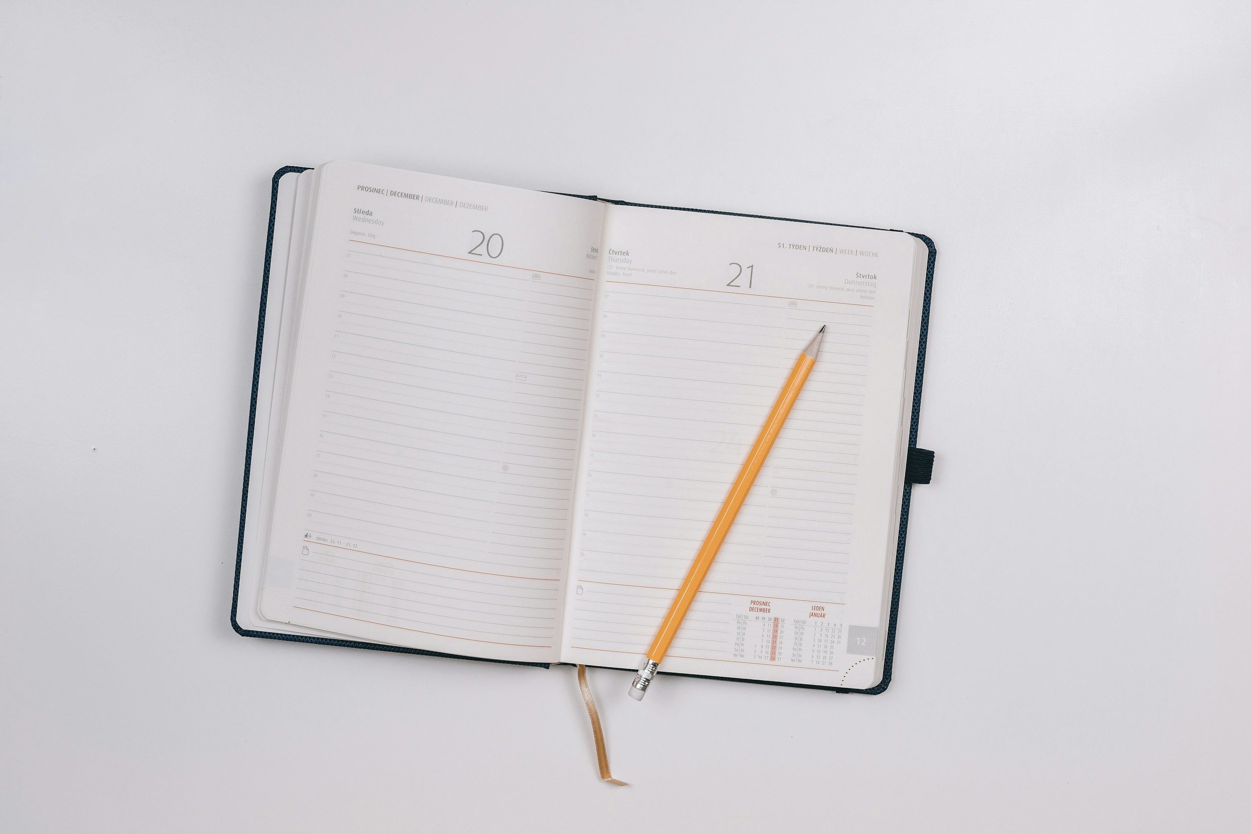 An open planner or diary with blank pages, displaying the dates Wednesday 20 and Thursday 21 of December, on a white surface with a yellow pen resting on it.