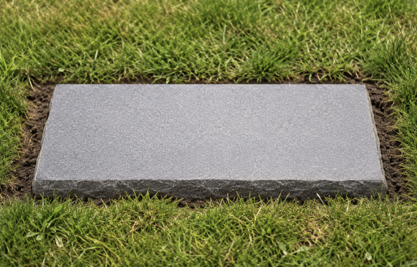 A rectangular gray stone plaque set in the ground, surrounded by green grass.