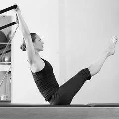 Woman in black workout clothes practicing yoga or pilates on a mat, raising her arms and legs in a pose.