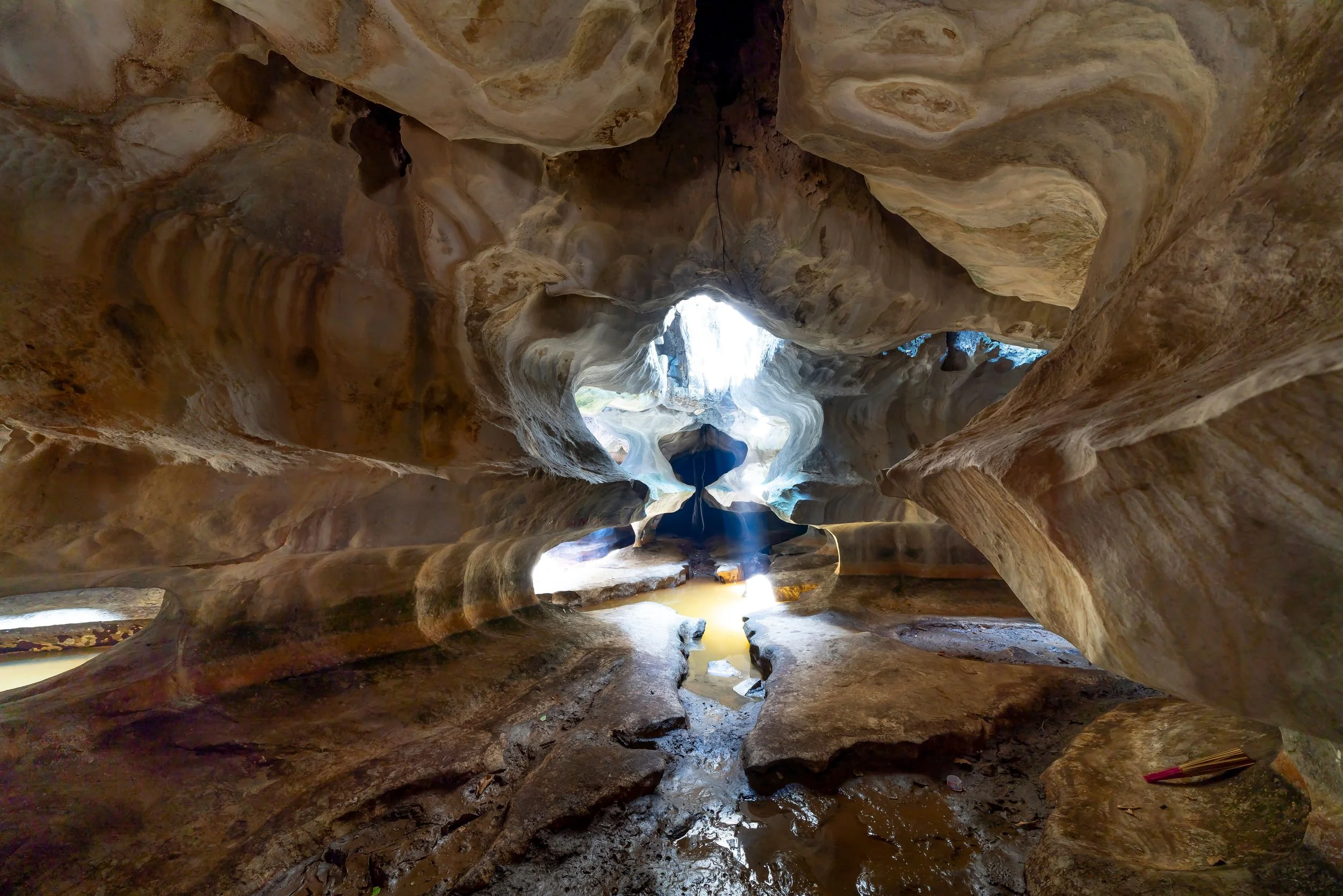 Inside view of a narrow, winding river with smooth, eroded rock formations on either side, sunlight filtering through the opening at the top.